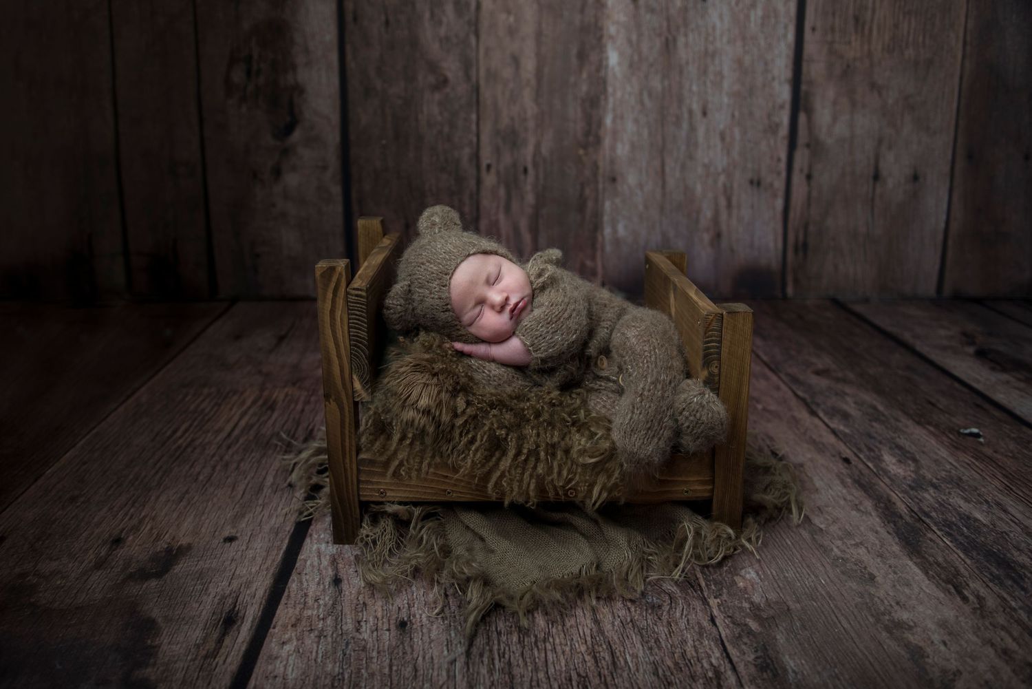Rustic newborn photography with vintage wooden floor and moody lighting.
