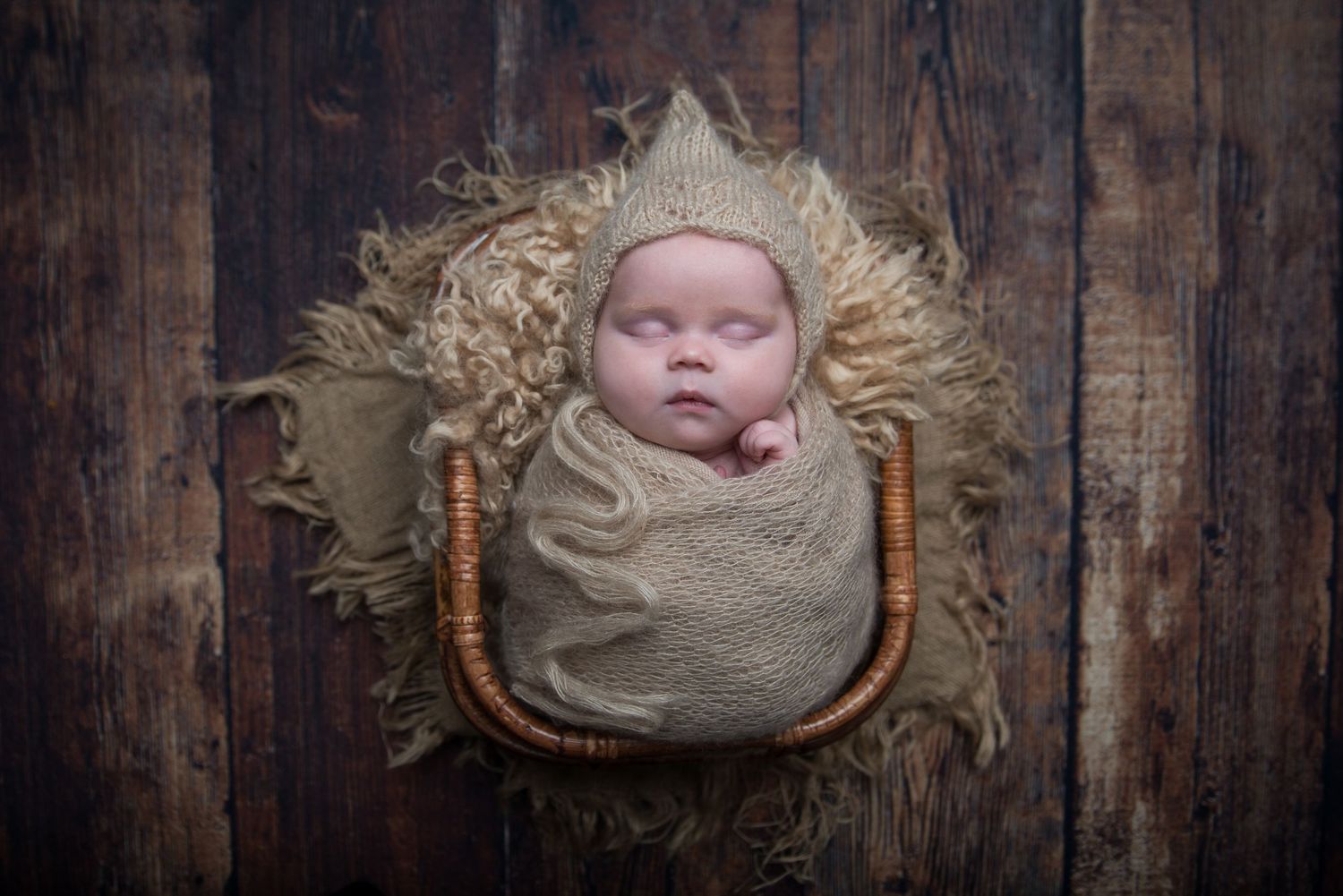 Artistic newborn portrait against dark wooden background with soft wrapping and rustic styling.