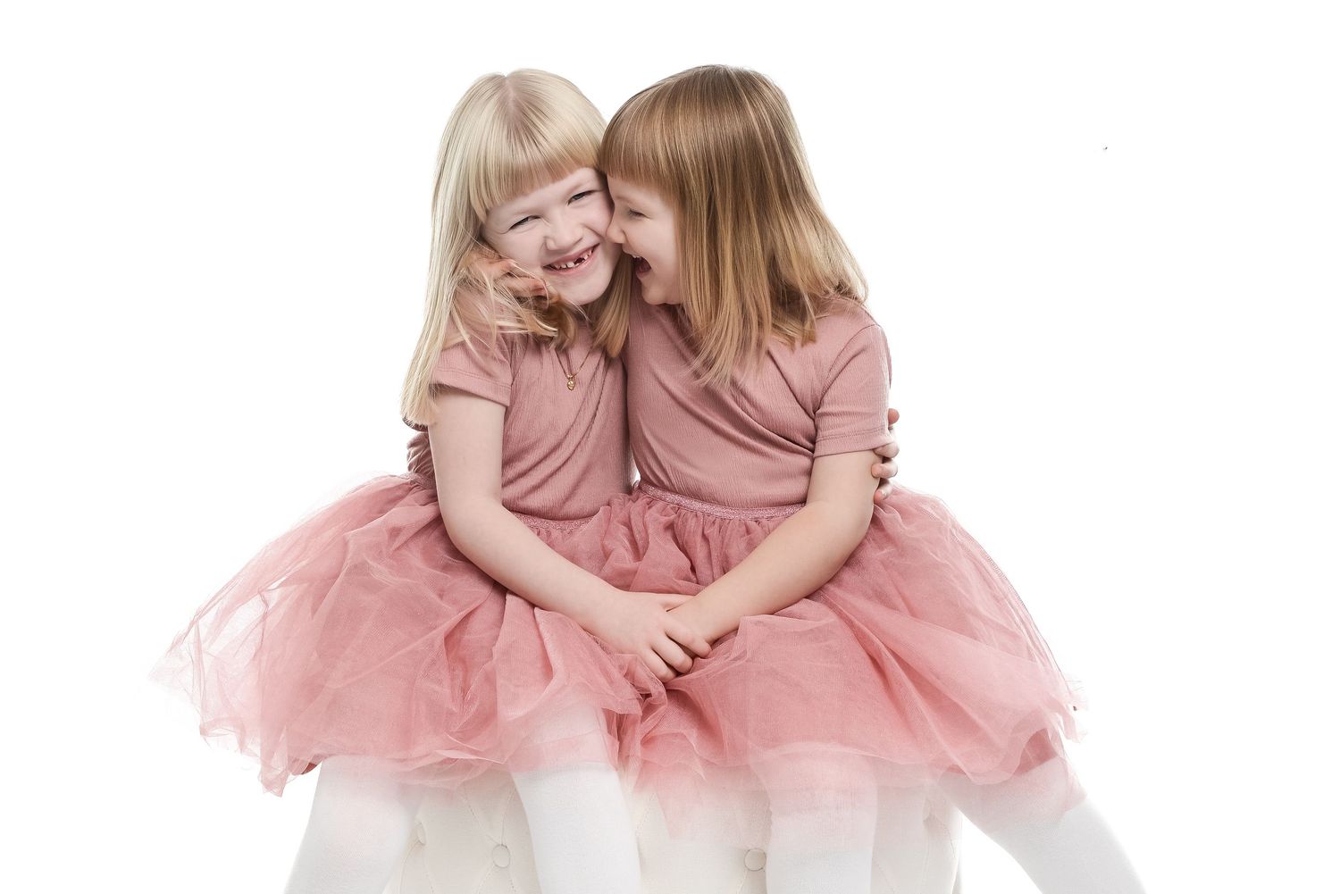 Two young children in pink tulle dresses pose playfully together on a white background.