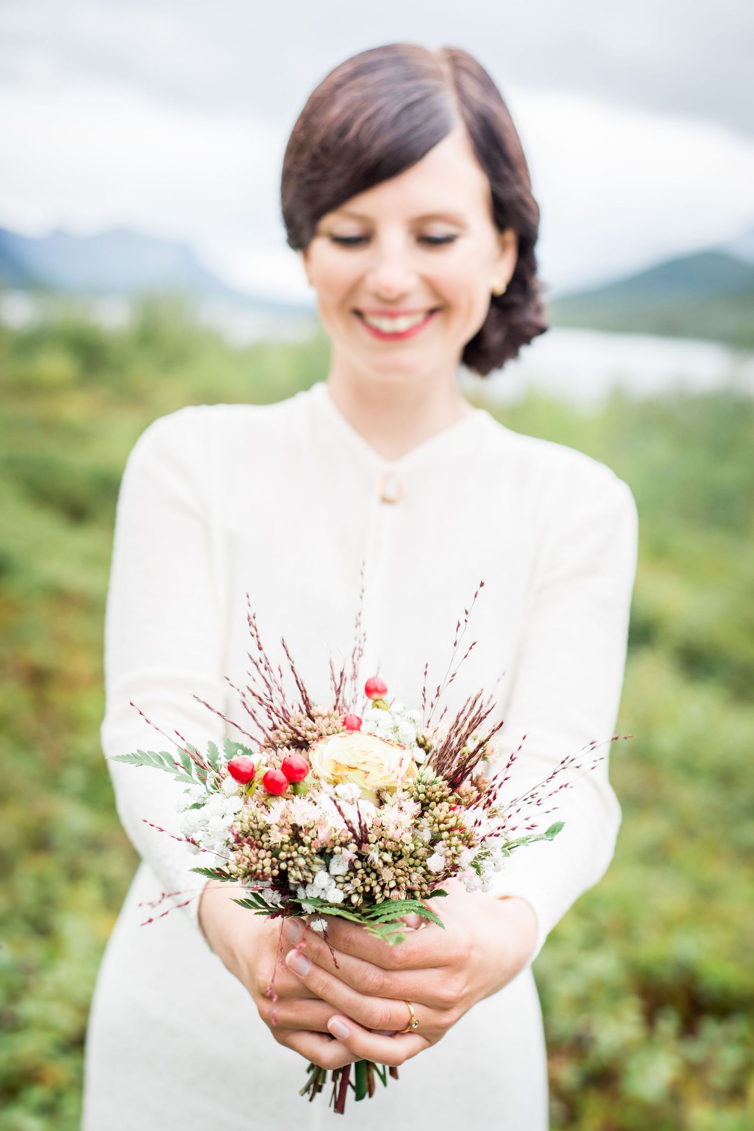 Elegant bridal bouquet with red berries and natural foliage photographed in series against mountain scenery.