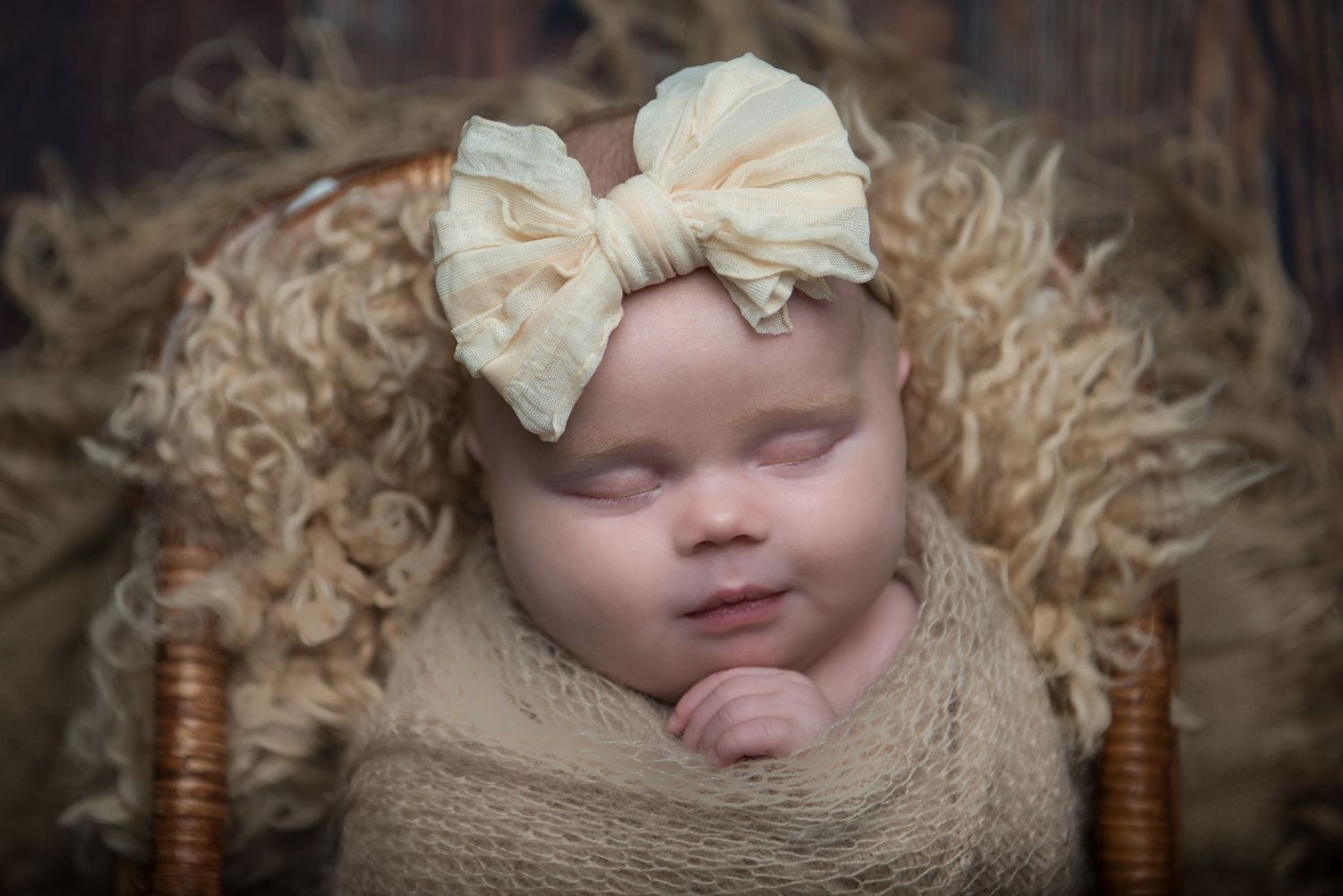 Delicate newborn portrait with cream bow accessory and natural straw styling elements.