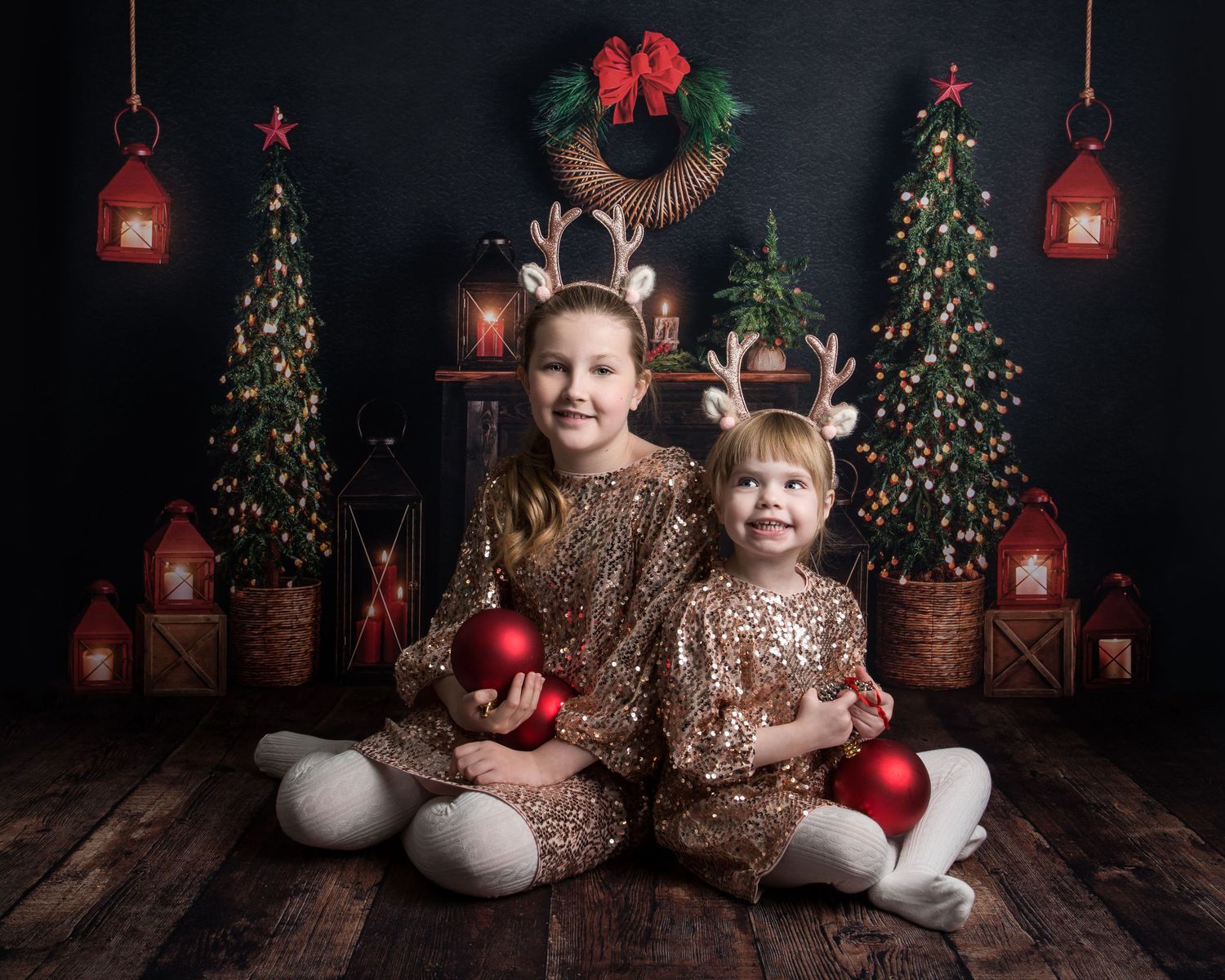 Christmas photo setup featuring red ornaments, wreaths, and glowing lanterns against a dark background.