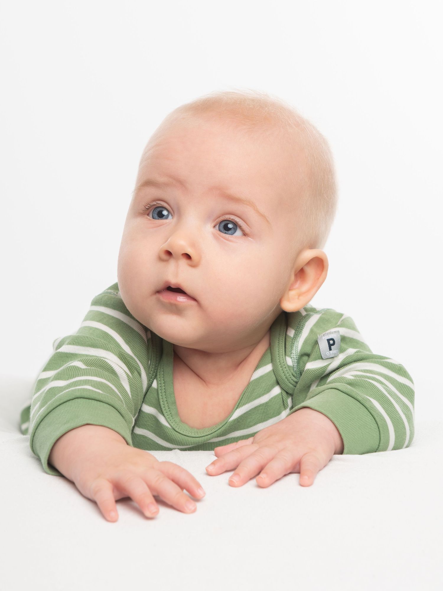 Baby in striped green outfit lying on white background looking up with bright eyes.