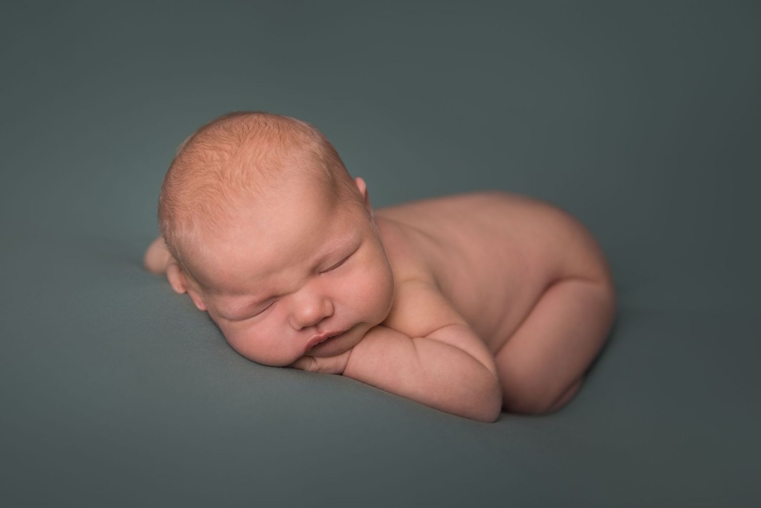 Side profile of sleeping newborn against sage green background in studio setting.