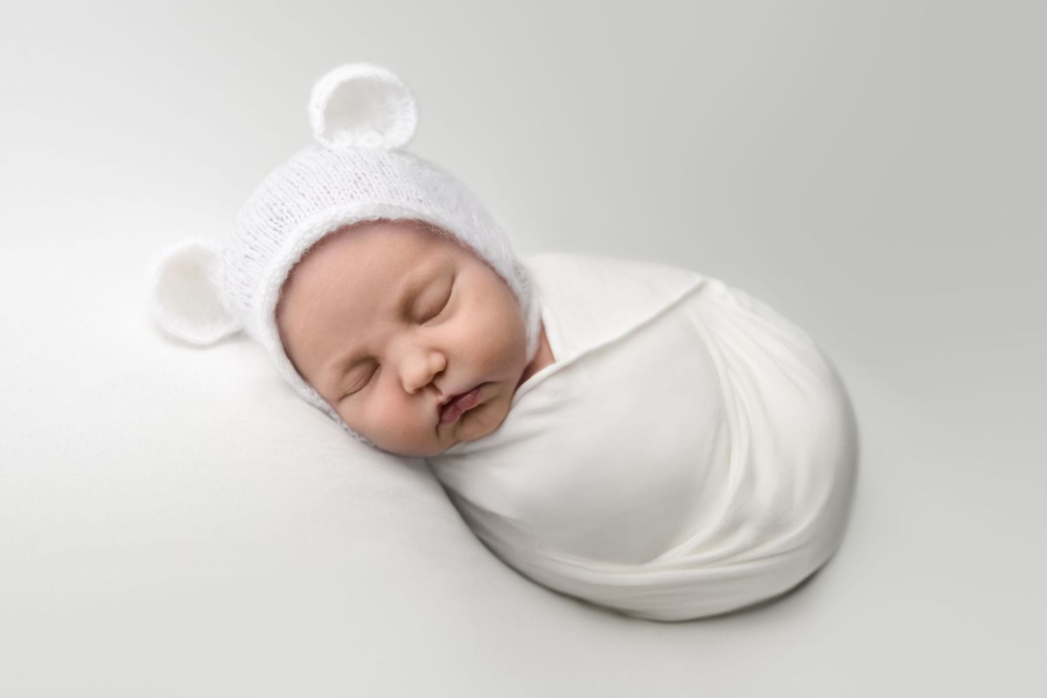 Serene newborn wrapped in white fabric on minimalist backdrop.