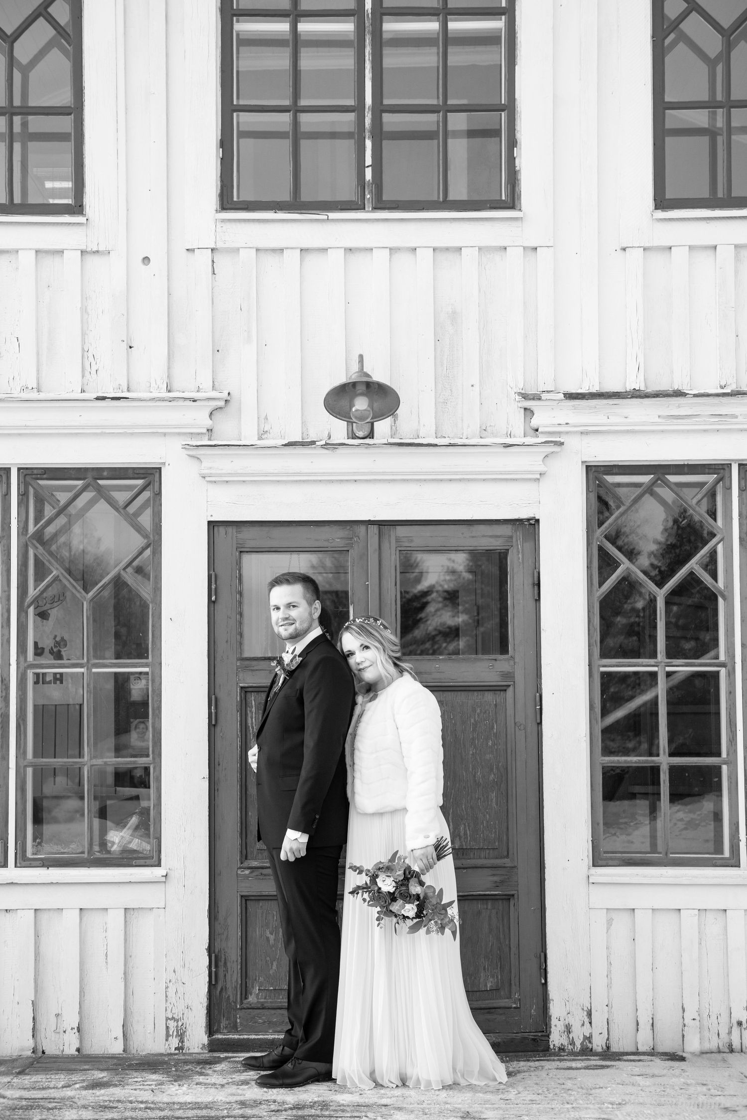 Wedding portraits against a white rustic building with vintage green doors and windows.