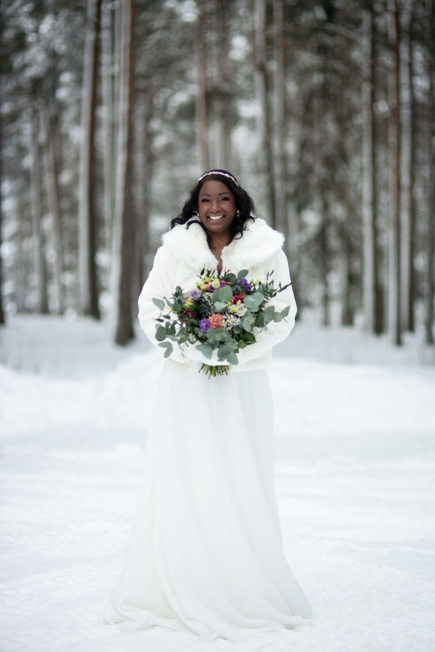 A bride poses in the snow wearing a flowing white dress and holding a vibrant floral bouquet.