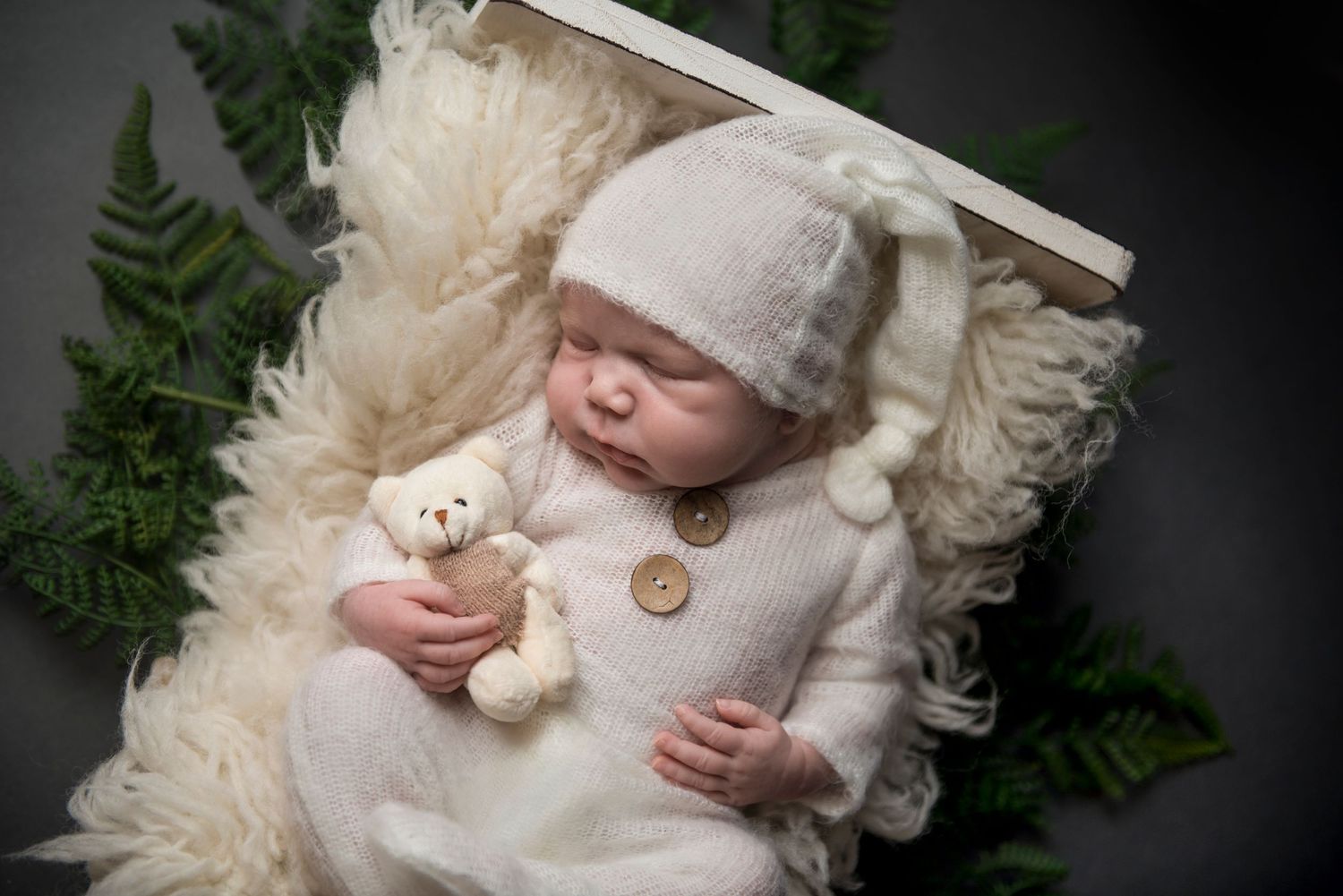 Newborn photography featuring white textured blanket and delicate greenery accents.