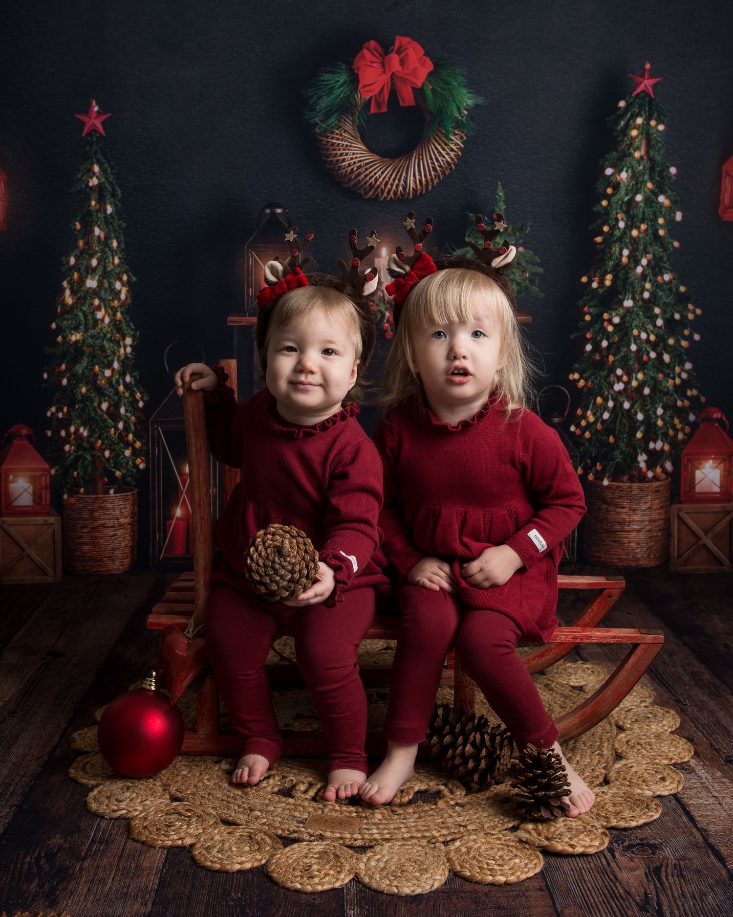 Christmas themed photo setup with decorated trees and pine cones on rustic wooden floor.