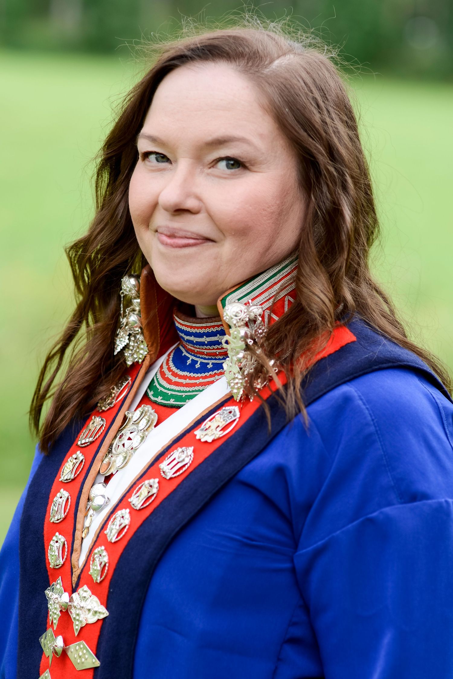 Woman in traditional Sami costume with colorful beaded necklace and silver jewelry, smiling outdoors.