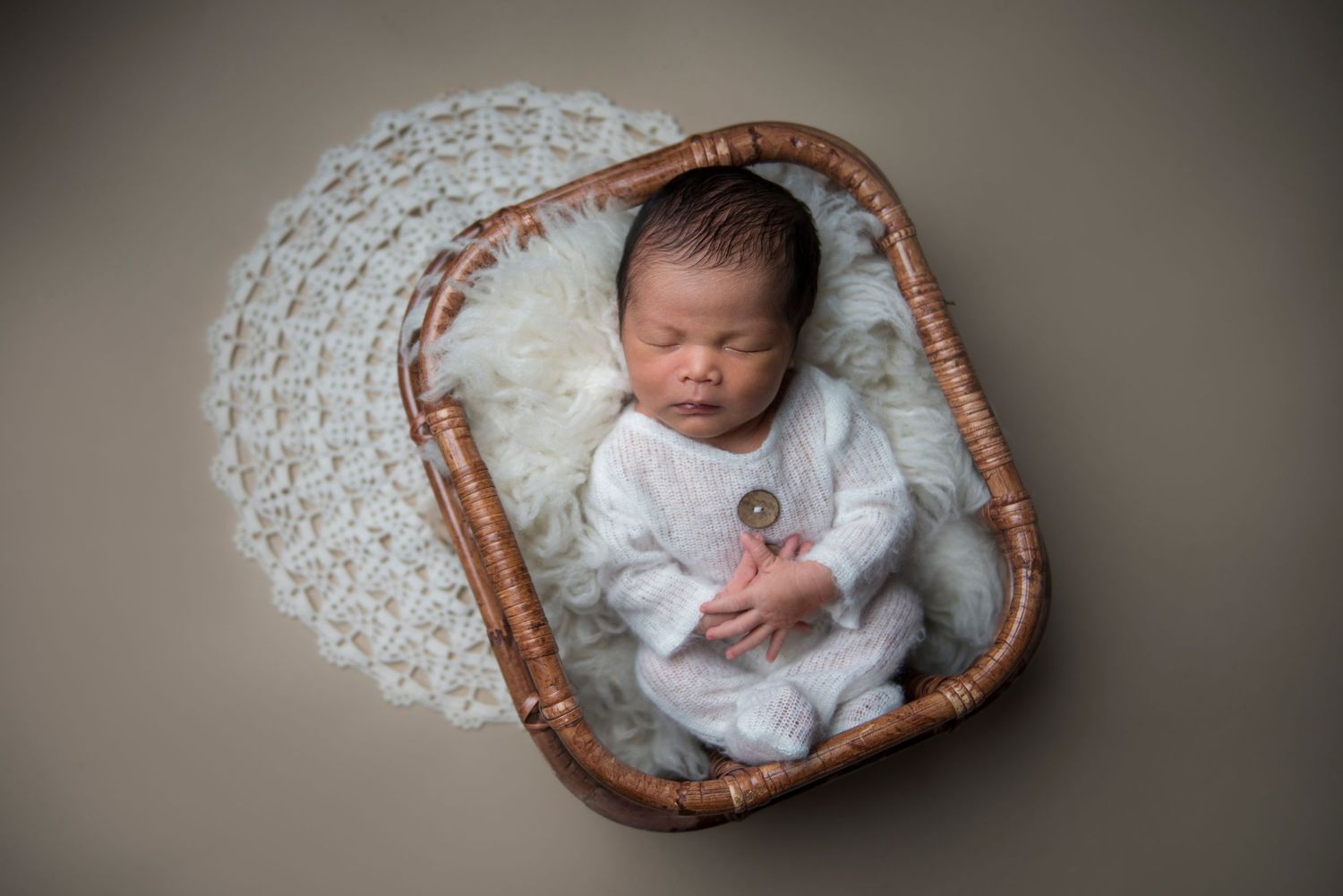 Newborn baby sleeping peacefully in a round woven basket with white lace trim.