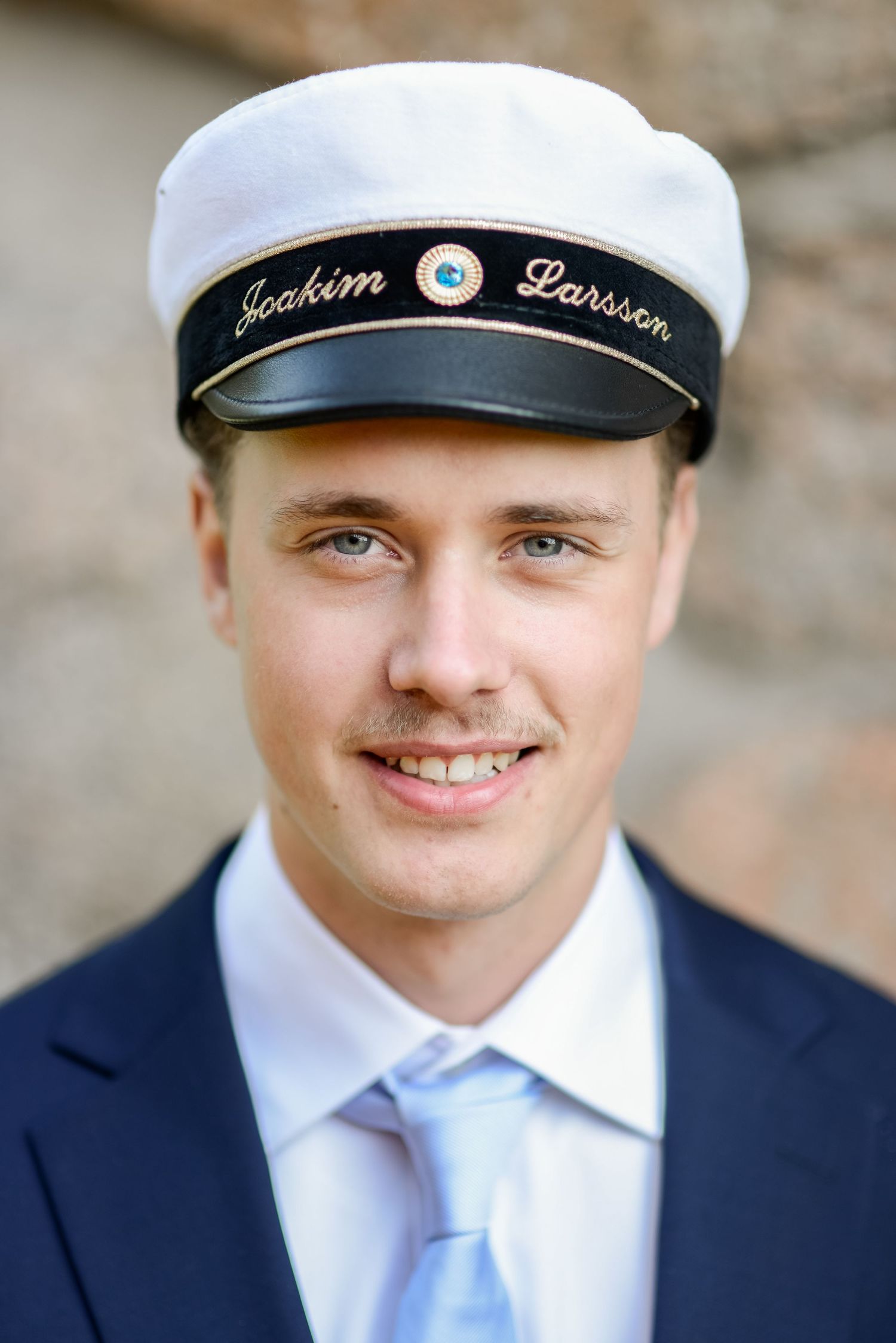 A graduate in a navy suit and sailor cap poses for a close-up portrait shot.