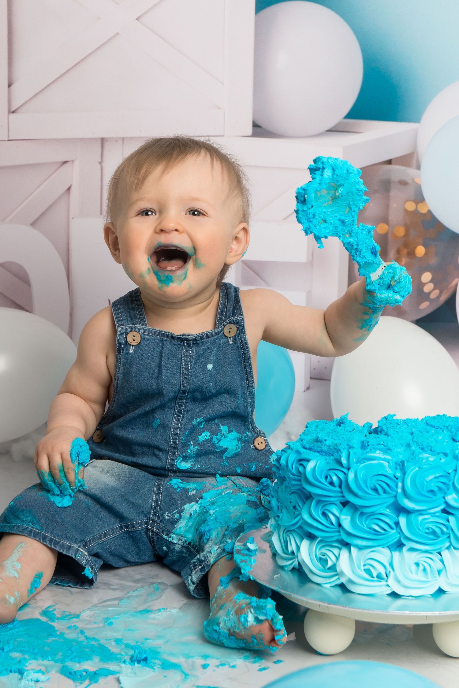 A cake smash photography session showing blue frosting mess and decorative white boxes in the background.