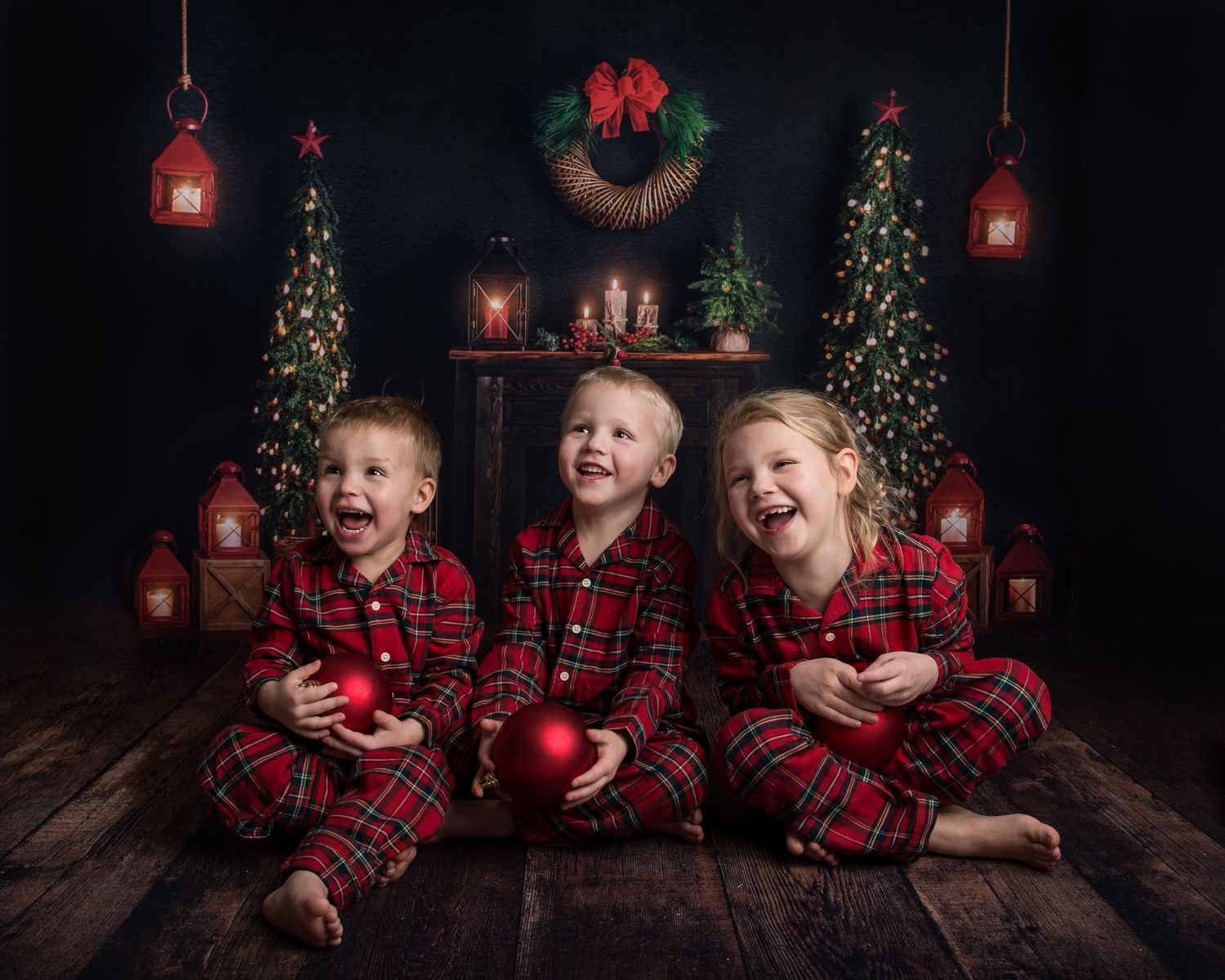 Children in matching plaid pajamas posing with Christmas decorations in a dark studio setting.