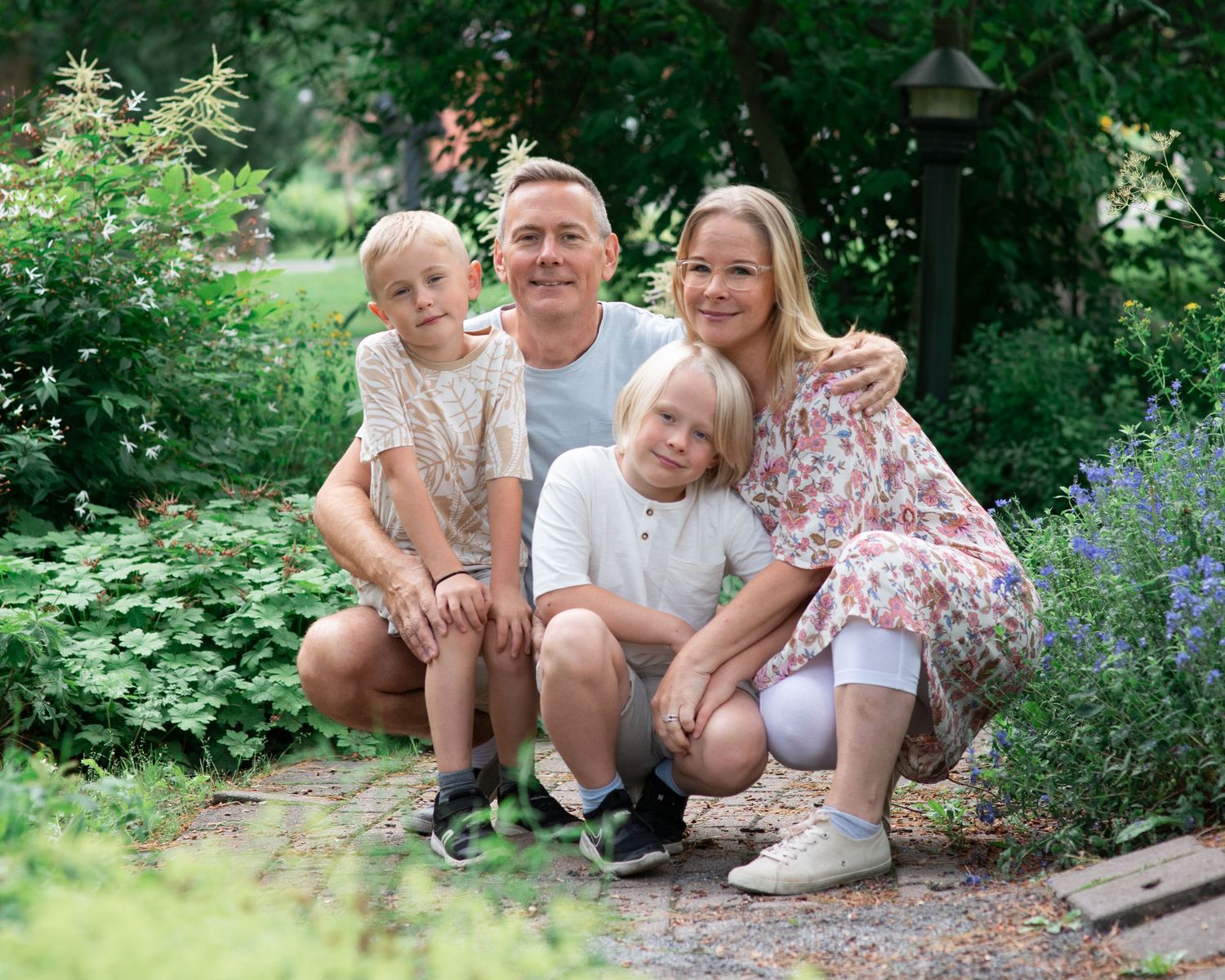 Happy family of four posing together in a lush green garden, smiling couple with two blonde children.