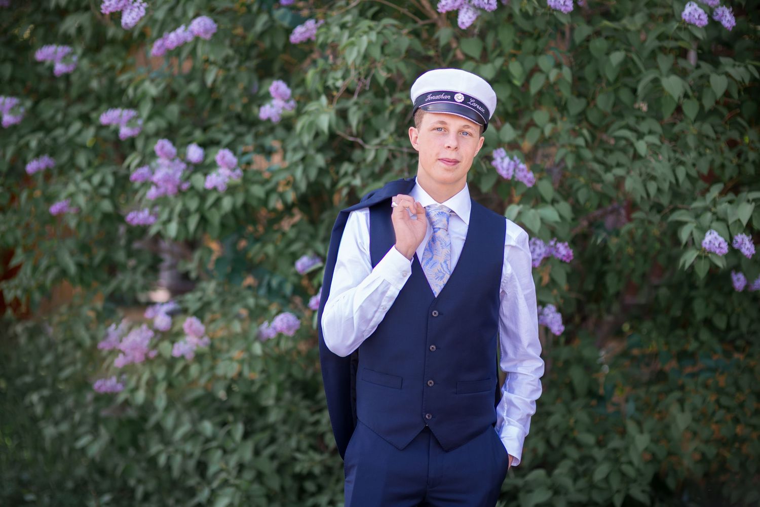 Portrait series against purple flowering bushes wearing formal navy vest and white shirt.