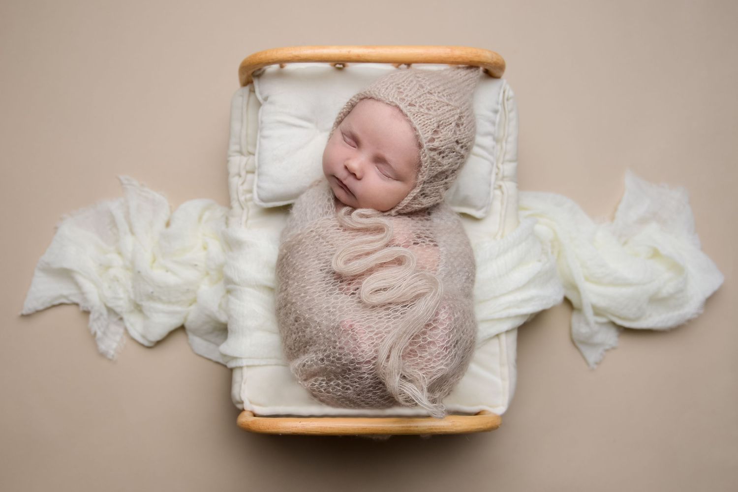 Baby sleeping in wooden basket with white fabric decorations.