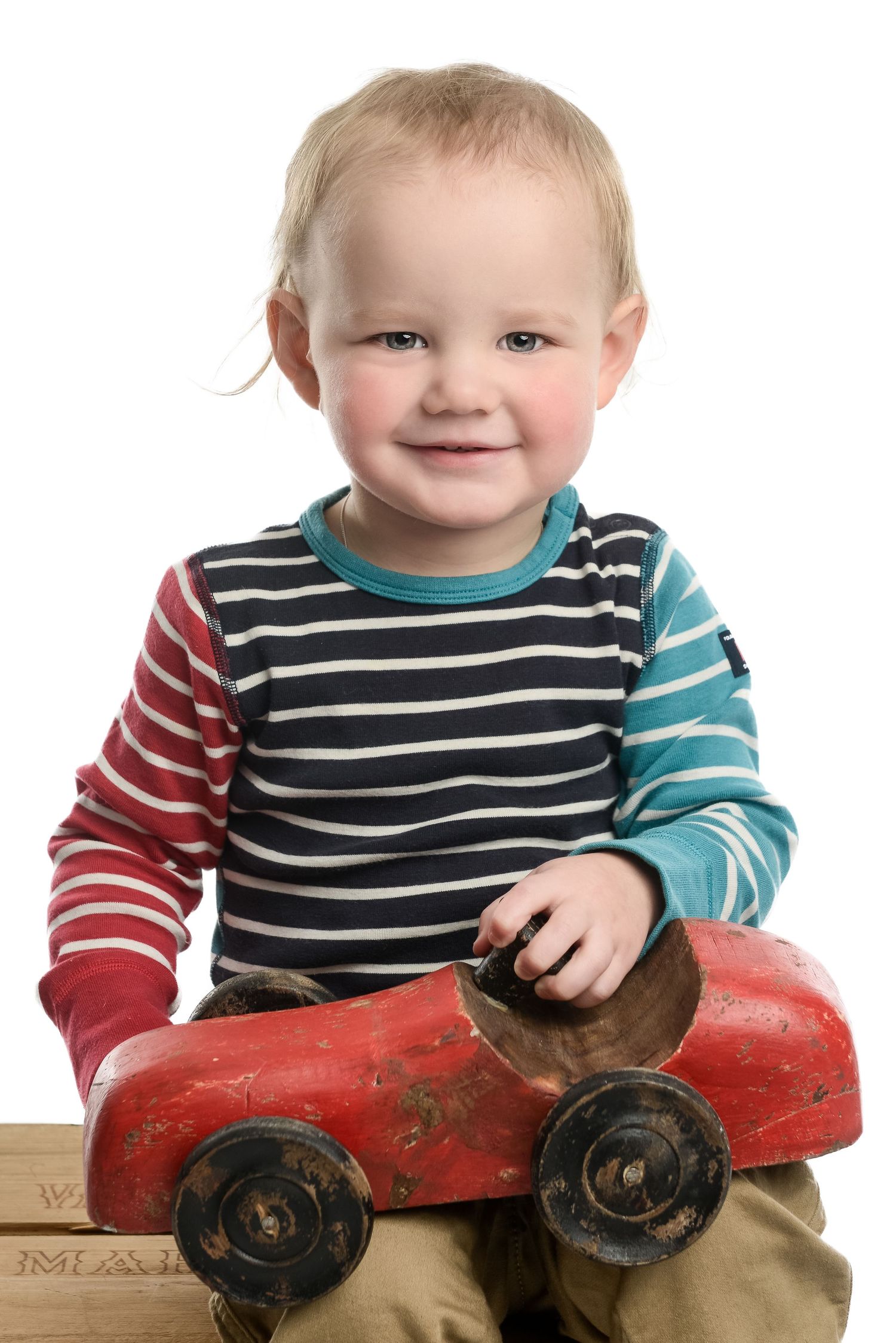 Child plays with antique red wooden toy while wearing colorful striped sleeves.