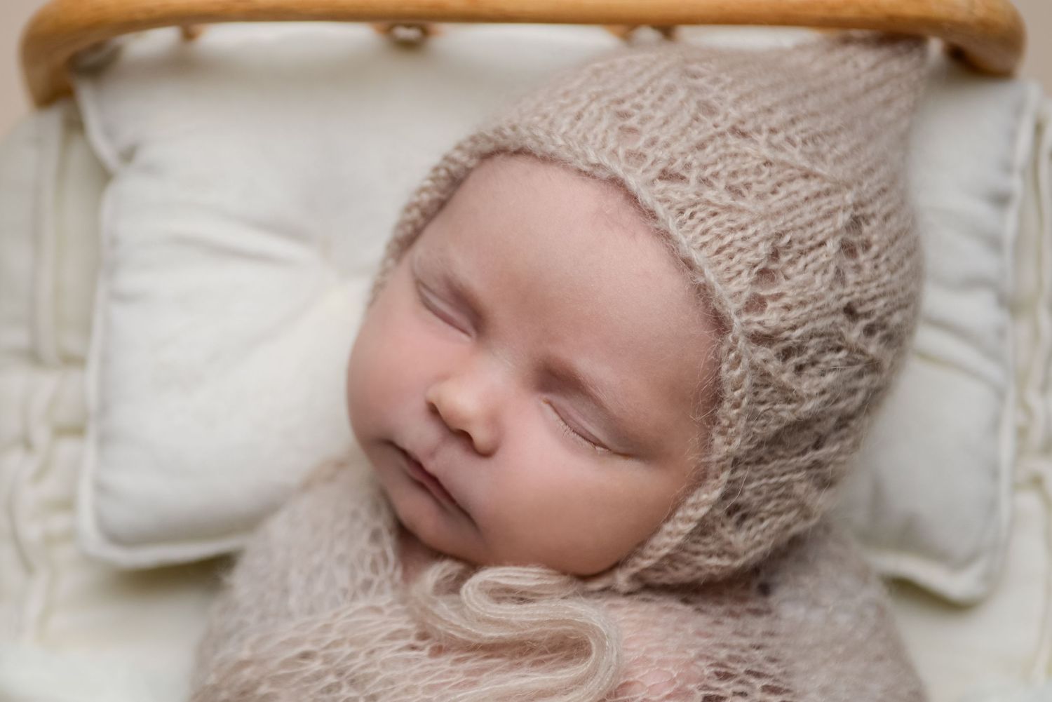 Baby wearing knit bonnet sleeping peacefully in vintage wooden basket.