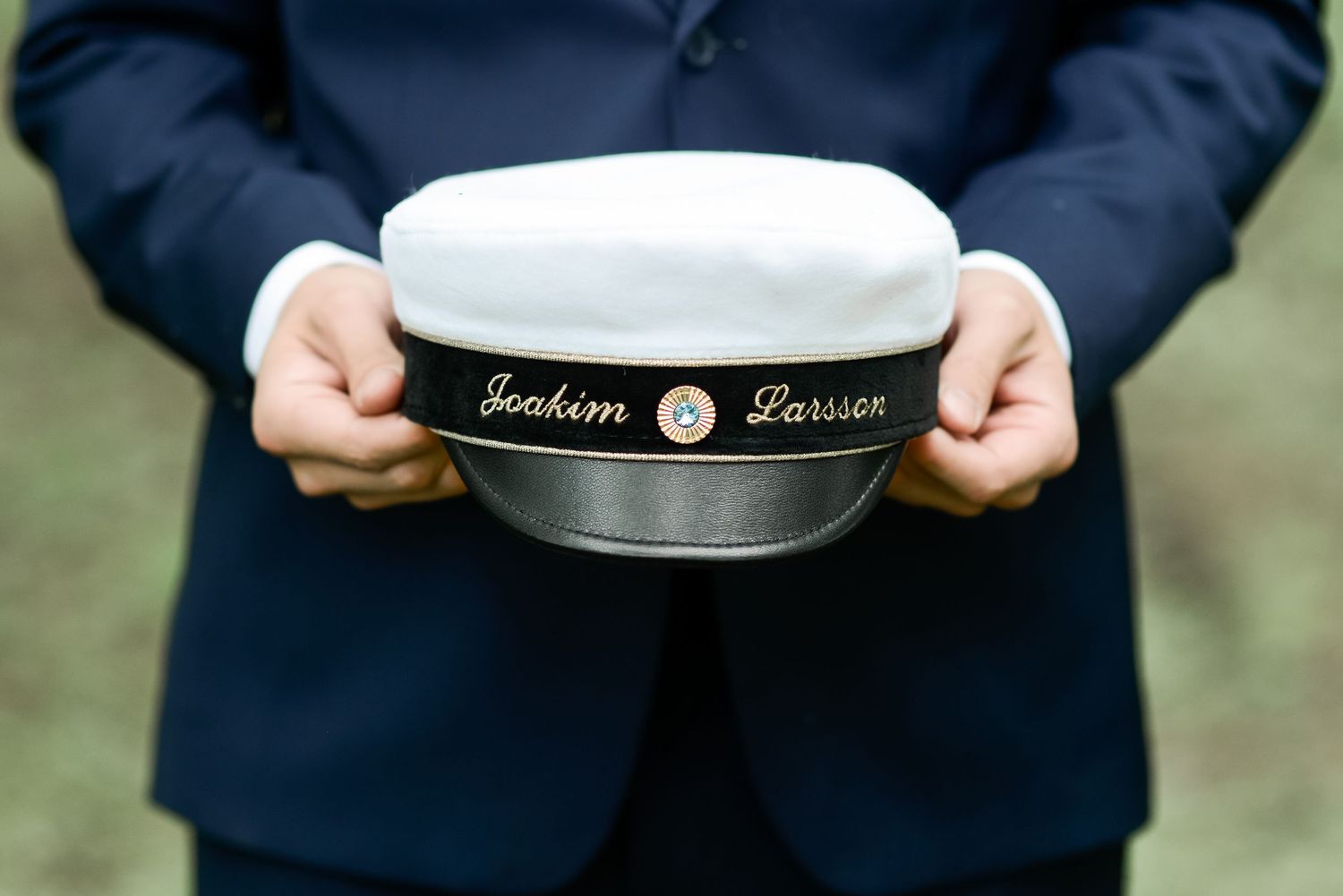 Close up of hands holding a white and black embroidered cap.