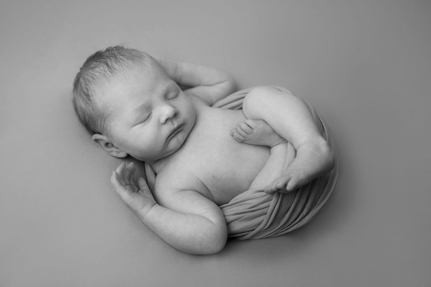 Peaceful newborn wrapped in soft fabric lying on neutral background.