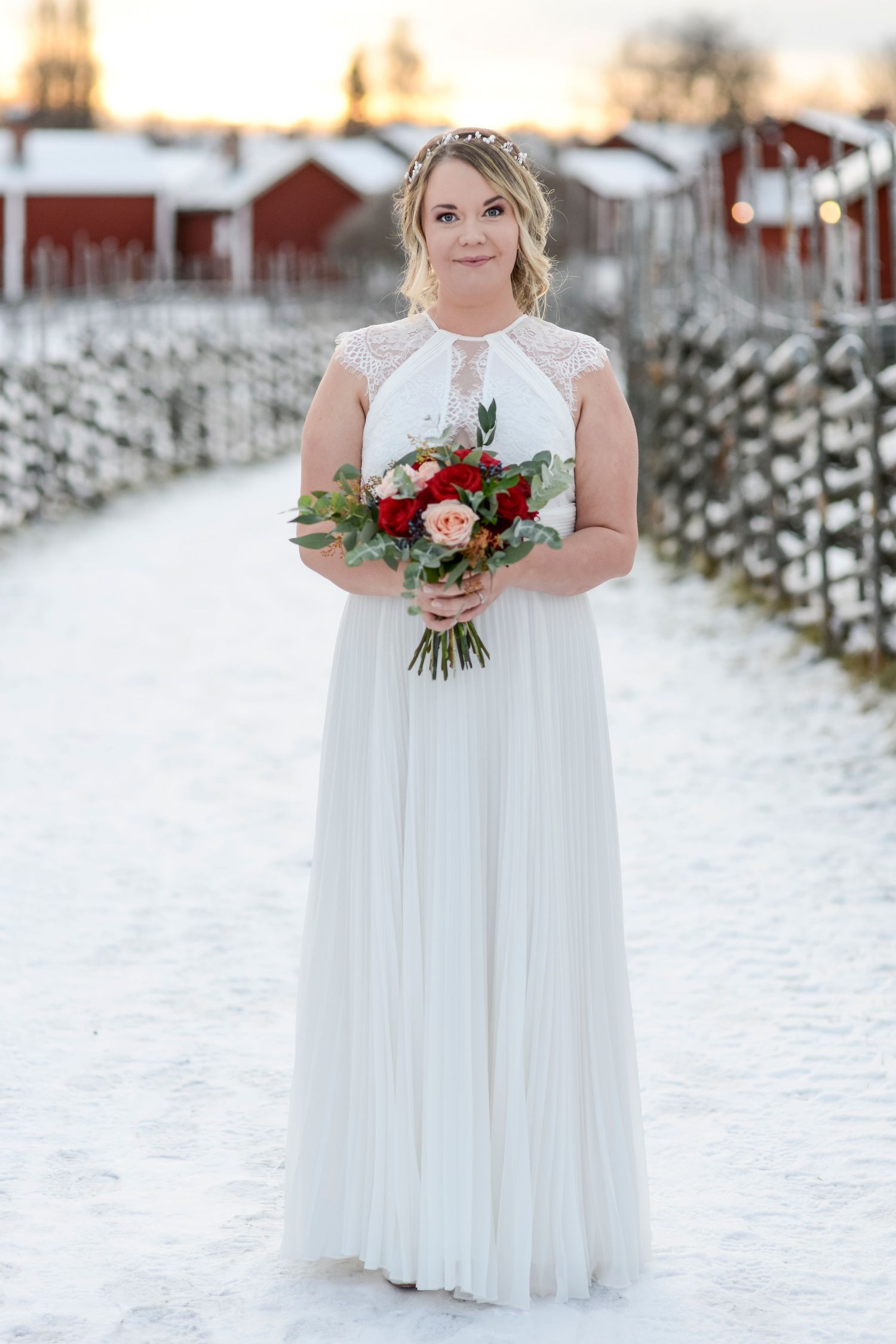 Bride in white dress holds a vibrant bouquet while standing in snowy winter landscape.