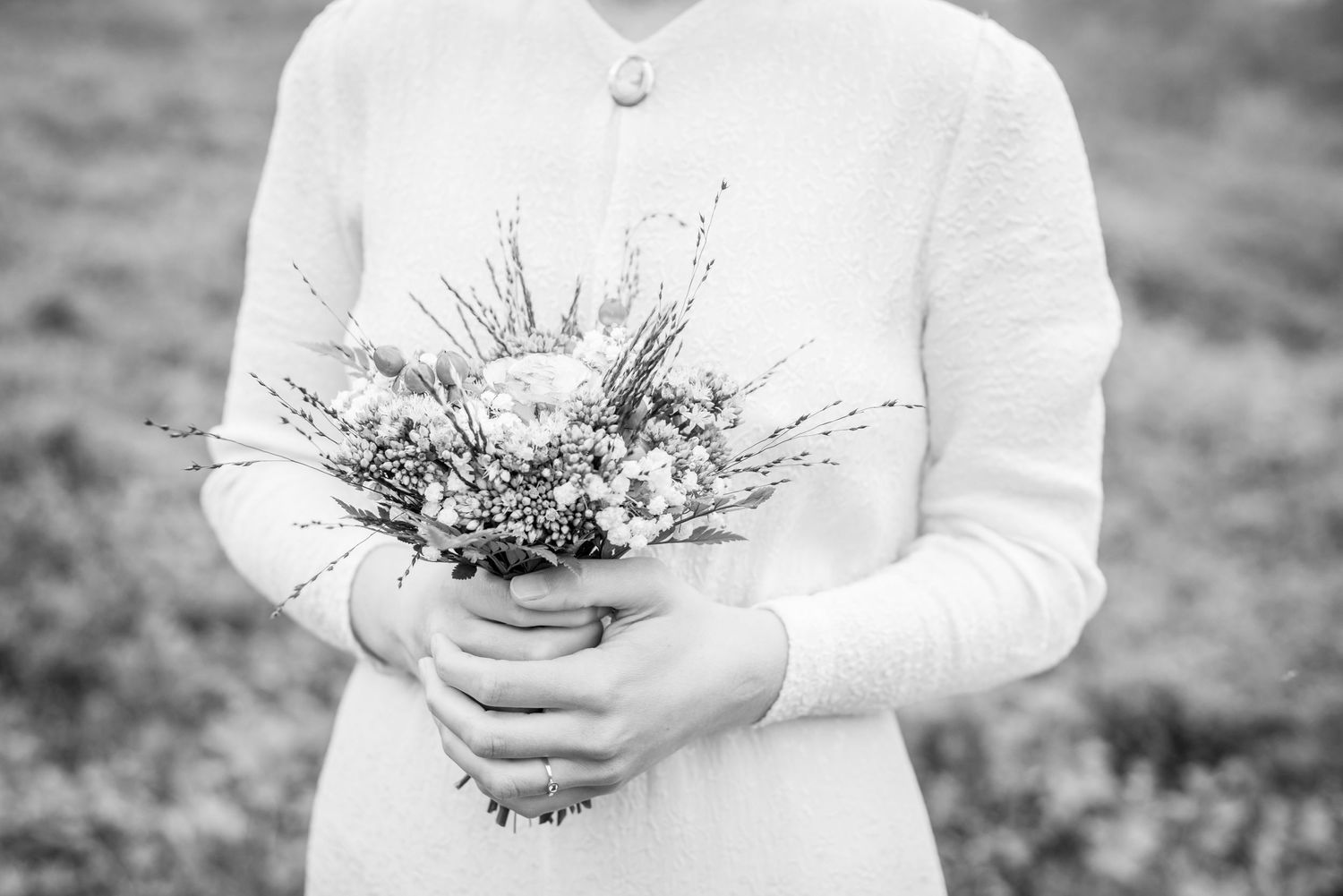 Black and white image of bride holding rustic bouquet in white long-sleeved dress.