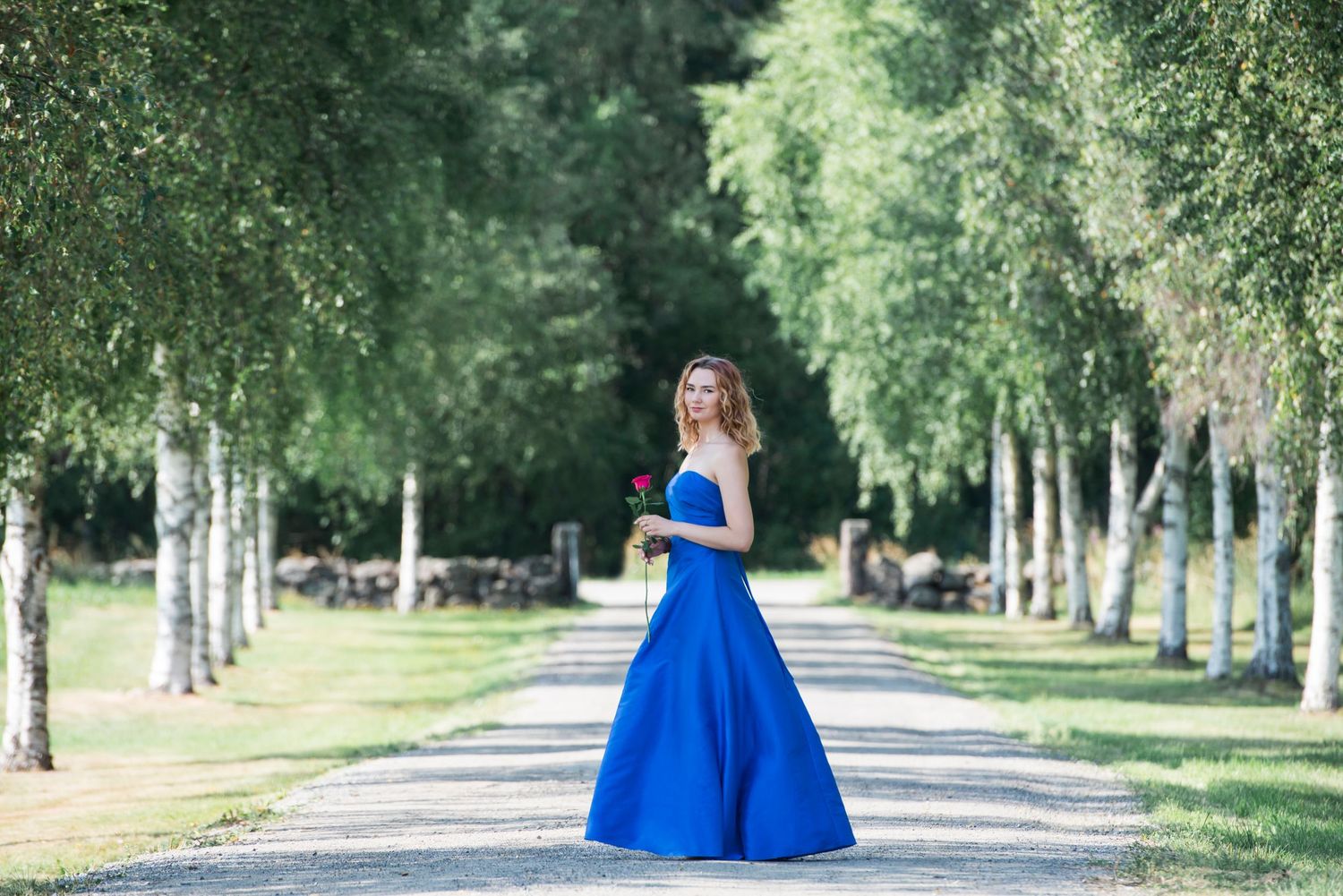 Tree-lined path with birch trees and a bright blue dress visible in the distance.