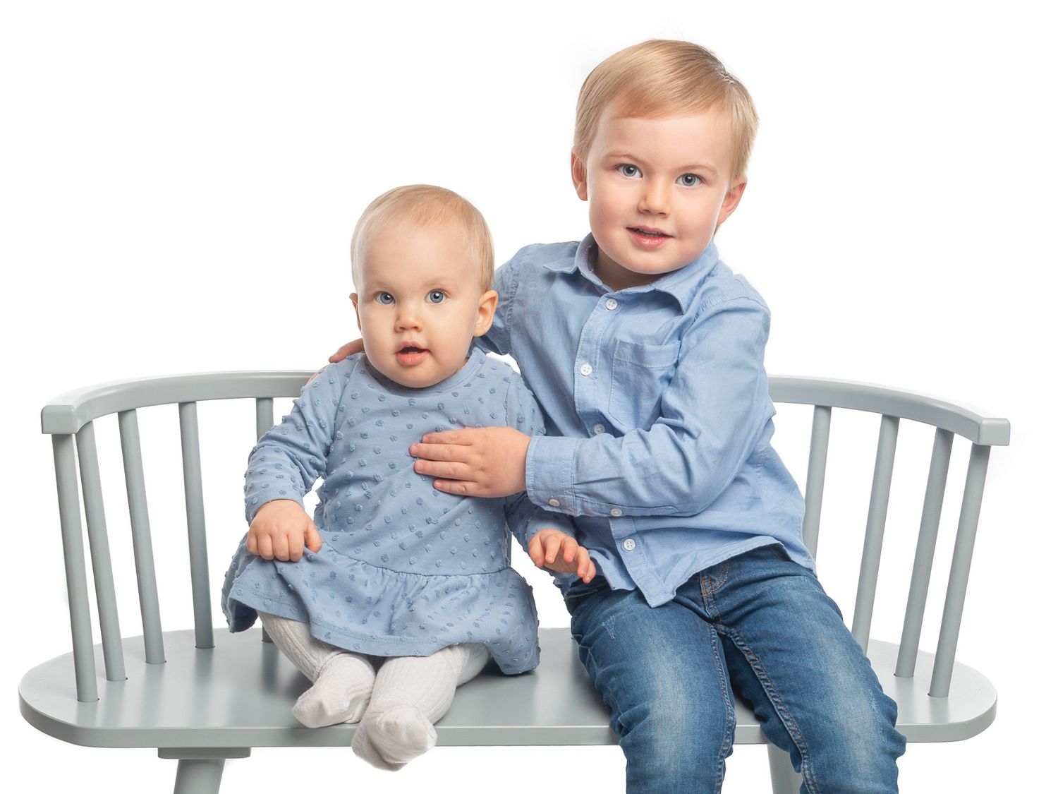 Two babies sitting on gray chairs wearing matching outfits.