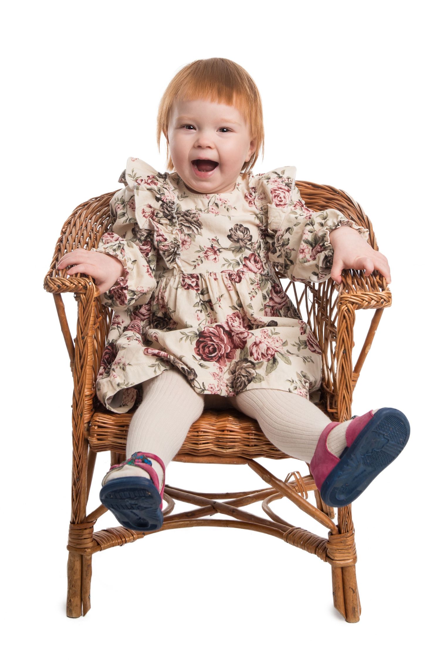 Sweet toddler wearing floral dress sits in wicker chair showing different playful expressions.