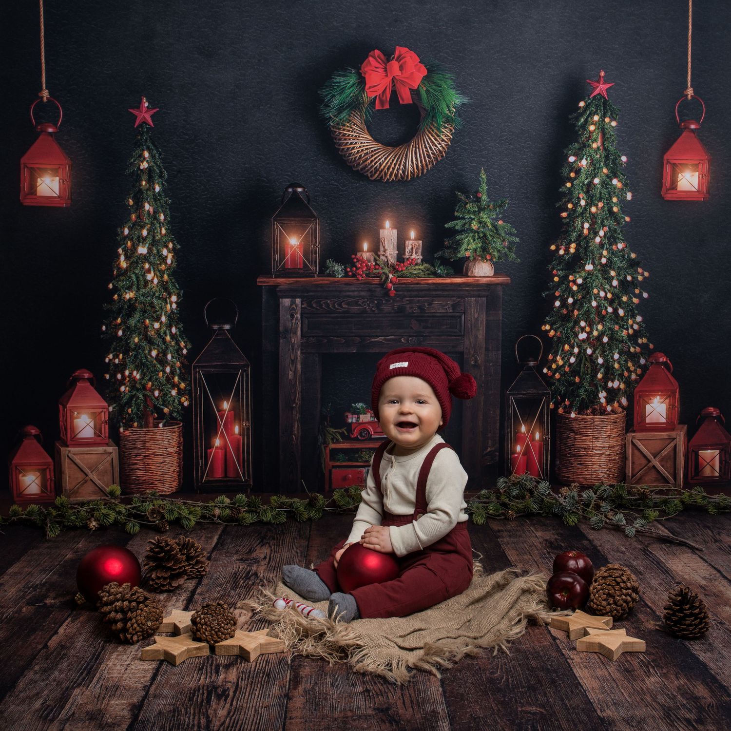 Christmas photo setup with decorated trees, red lanterns, and rustic wooden floor in dark moody setting.