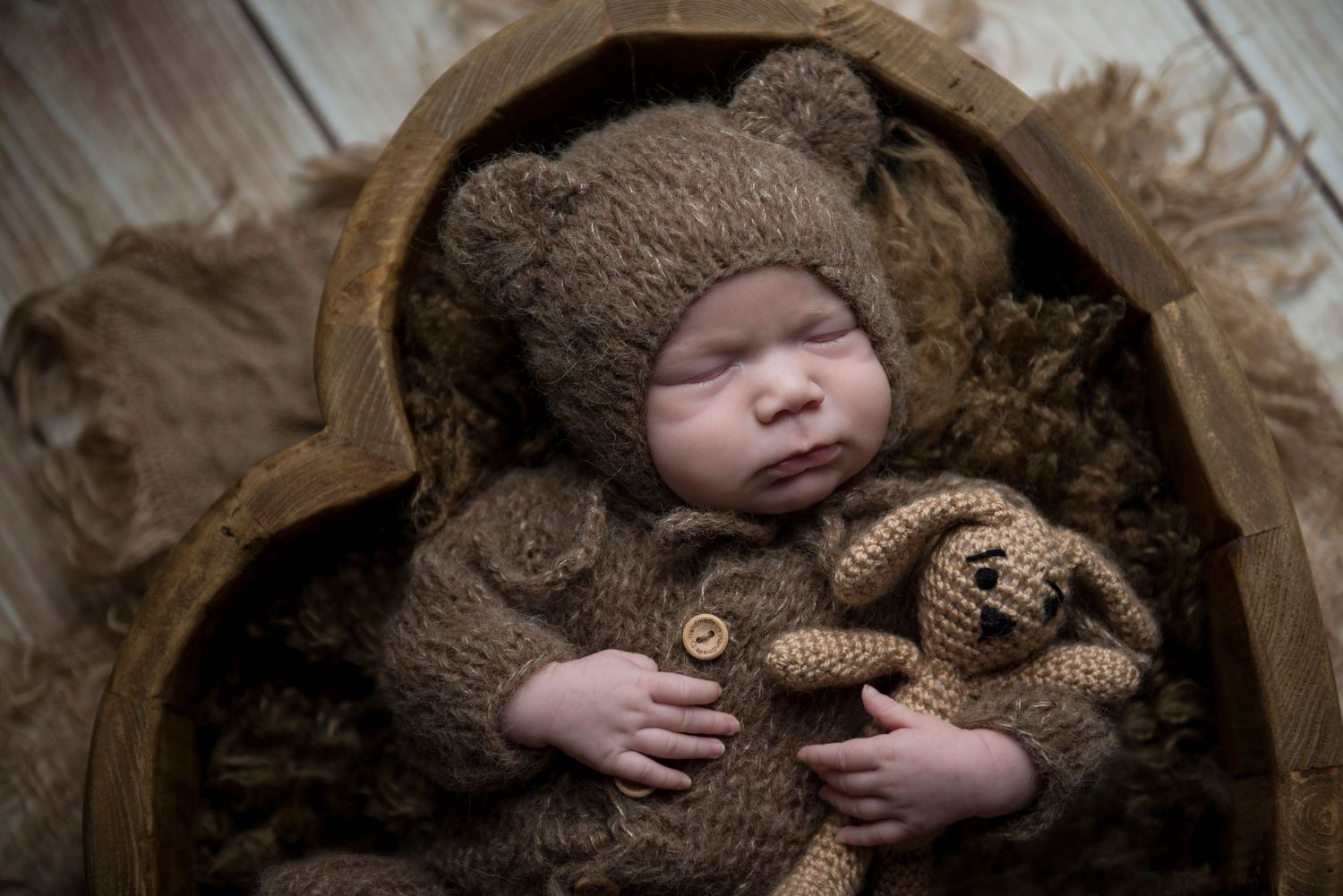 Professional newborn portrait with cozy brown blanket and teddy bear prop.