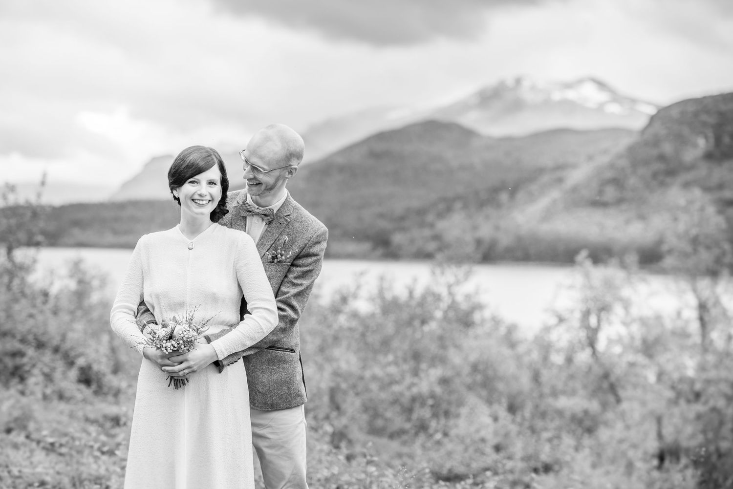 Black and white photo of a couple's tender moment with dramatic mountain scenery.