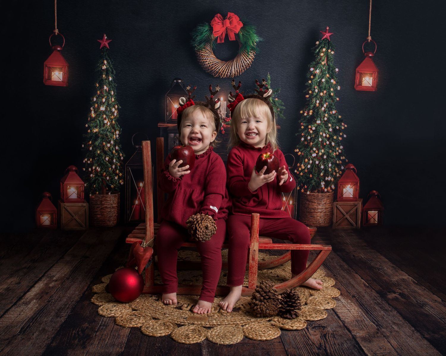 Holiday photo setup with decorated Christmas trees, red lanterns and rustic wooden floor.