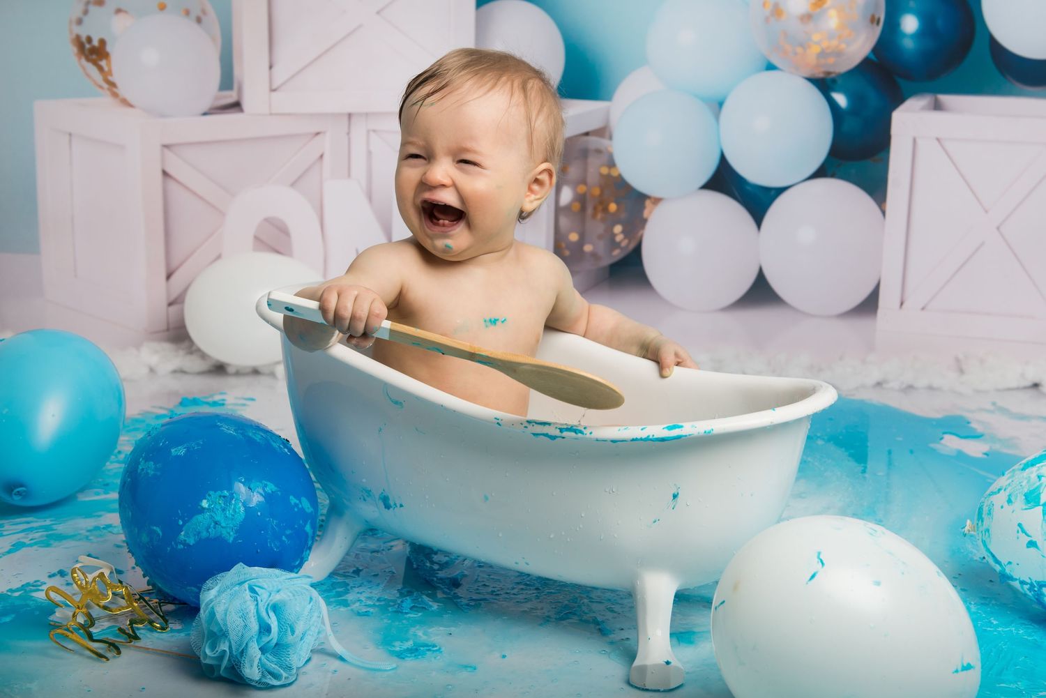 A joyful cake smash session featuring a white bathtub and blue decorations against a balloon backdrop.