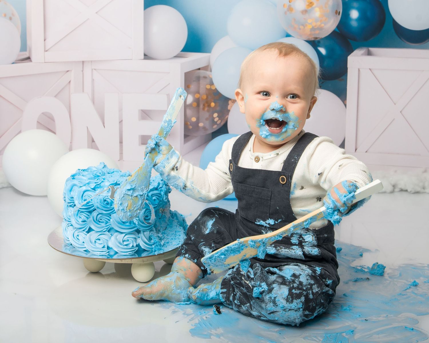 Blue cake smash photography session with messy frosting and decorative balloons.
