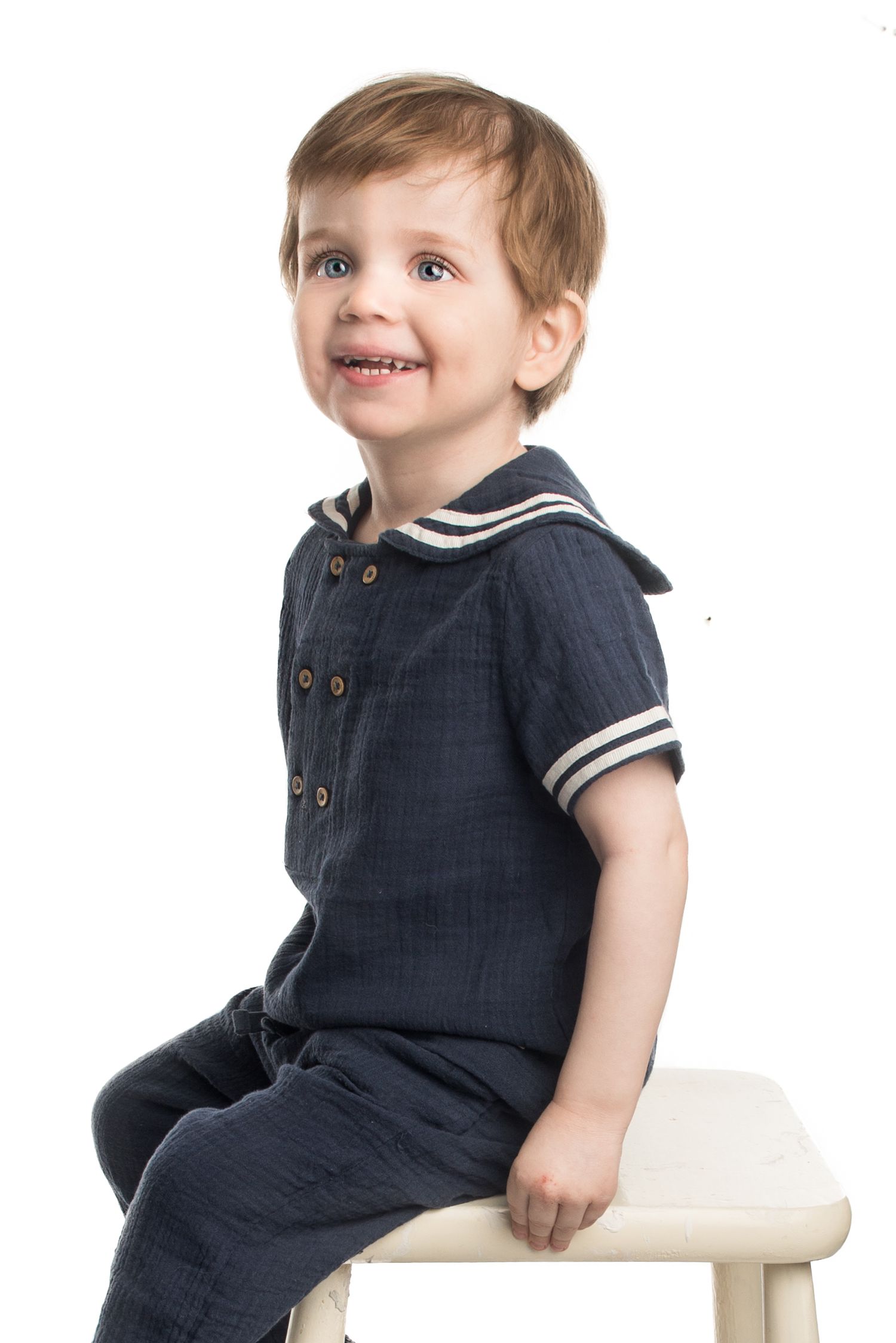 Child in navy sailor outfit sits on white bench during portrait session.