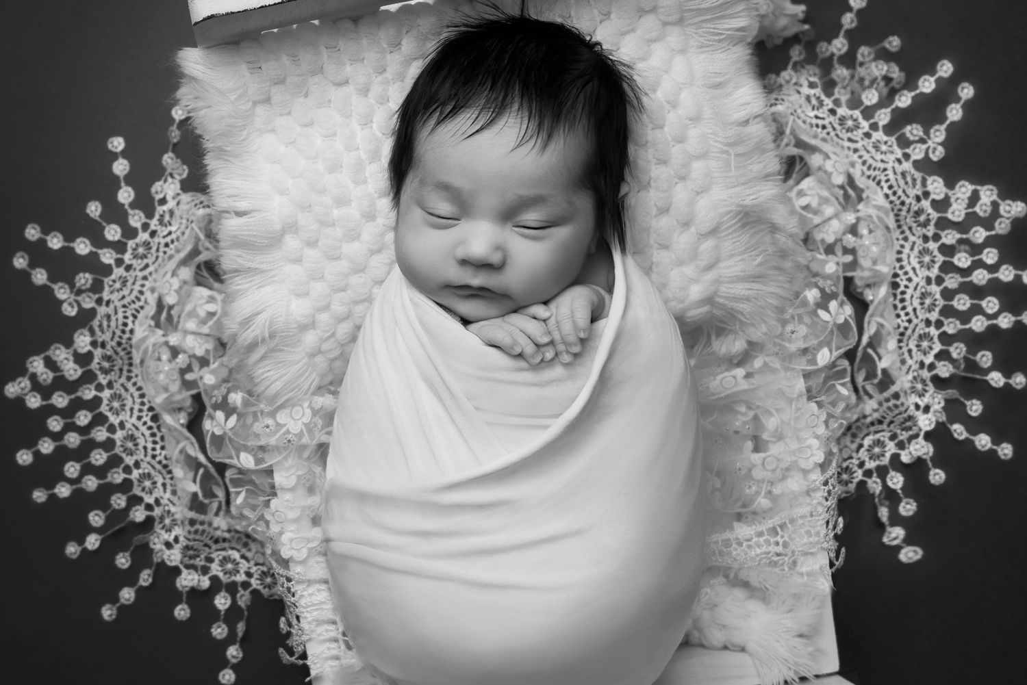 Swaddled newborn on white pillow surrounded by delicate pearl decorations in black and white.