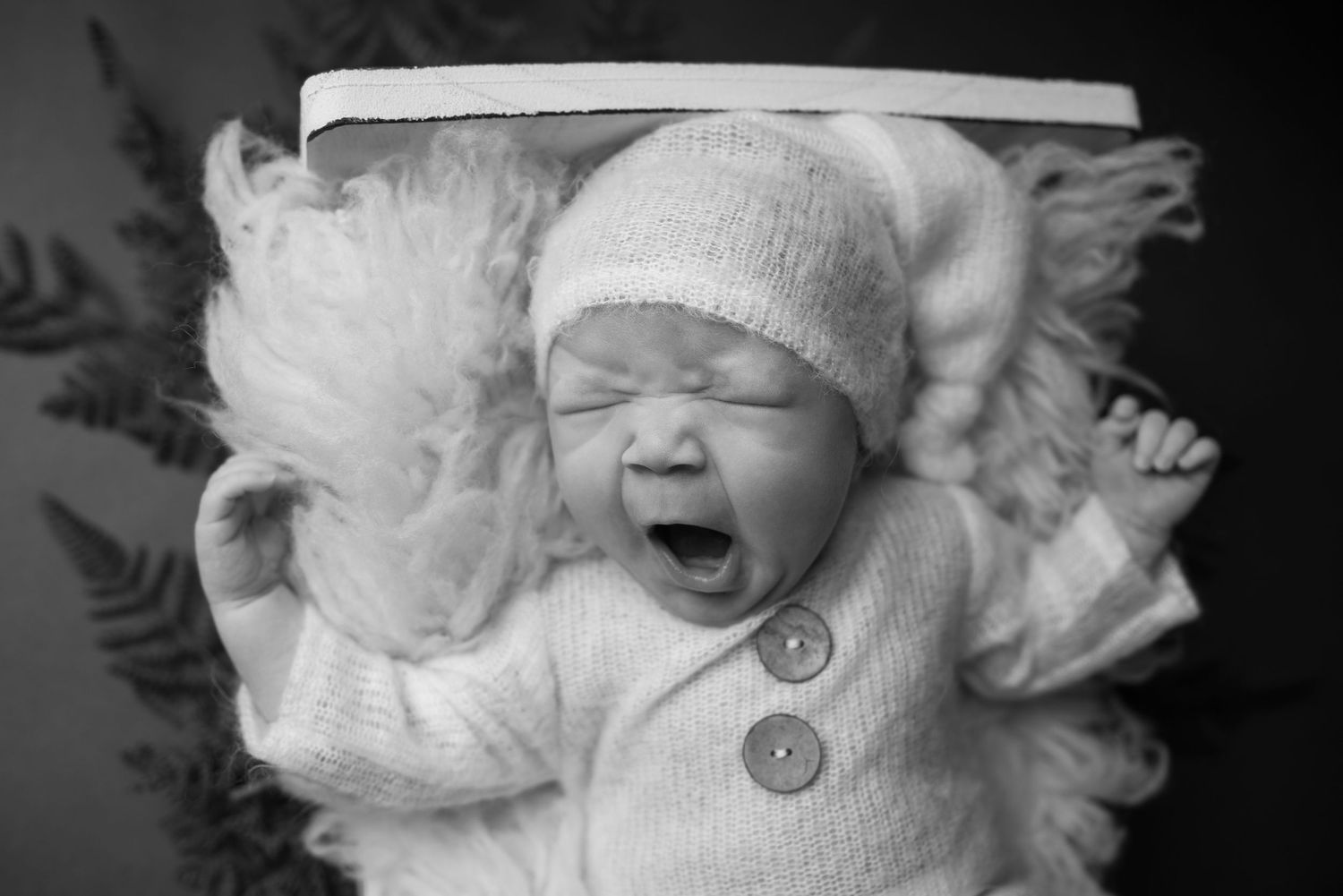 Close-up portrait of a sleeping newborn wearing a white knit hat with decorative buttons.