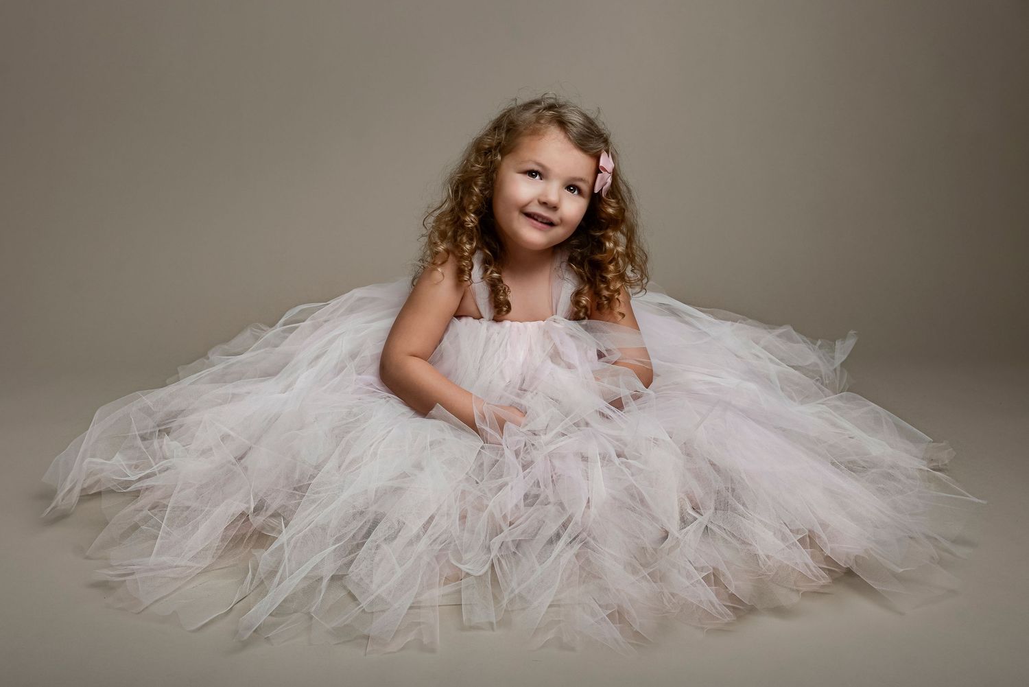 Graceful pose in delicate tulle dress creating romantic studio portrait.