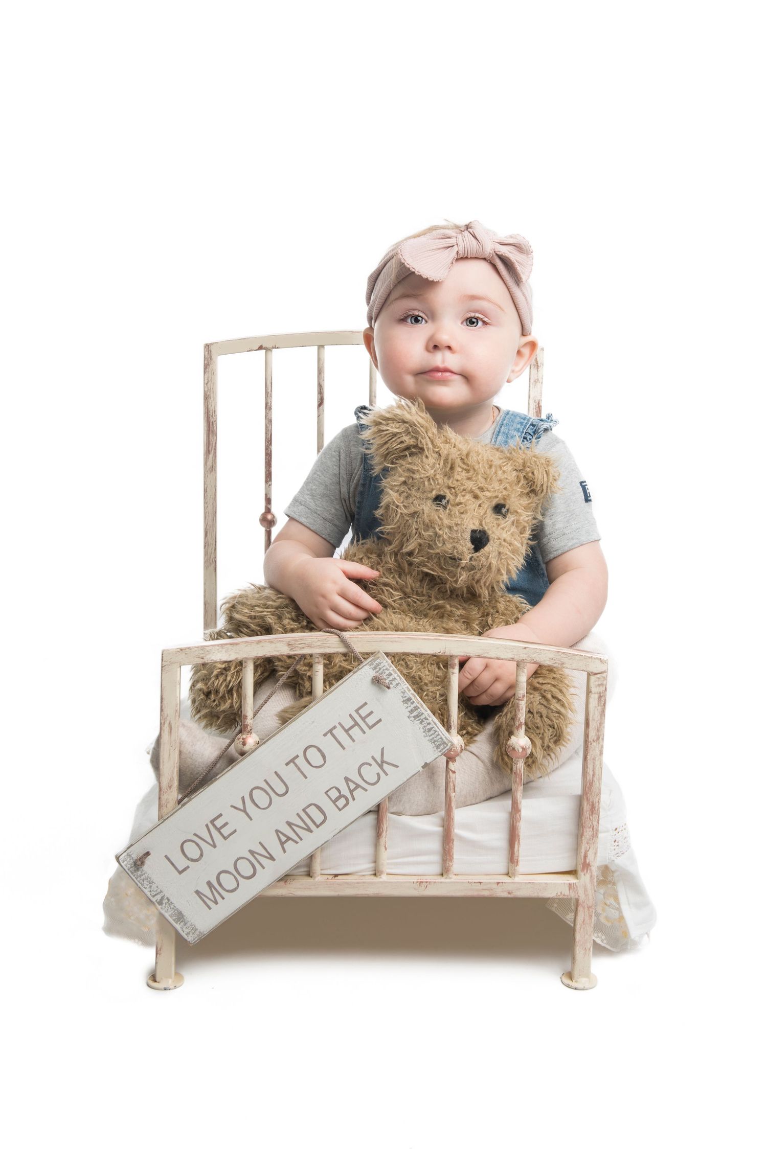 A young child in denim sits with a teddy bear on a rustic wooden bench with text.