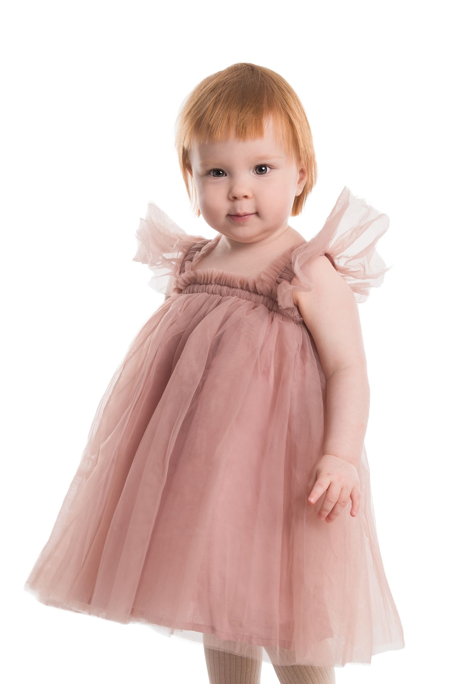Toddler wearing pink tulle dress poses against white background.