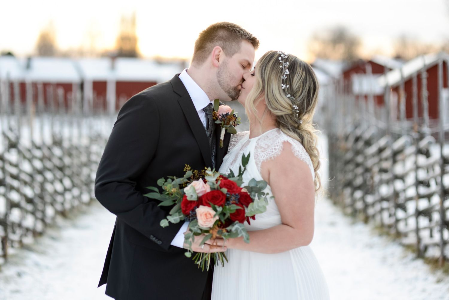 A winter wedding couple shares an intimate moment in the snow with a red floral bouquet.