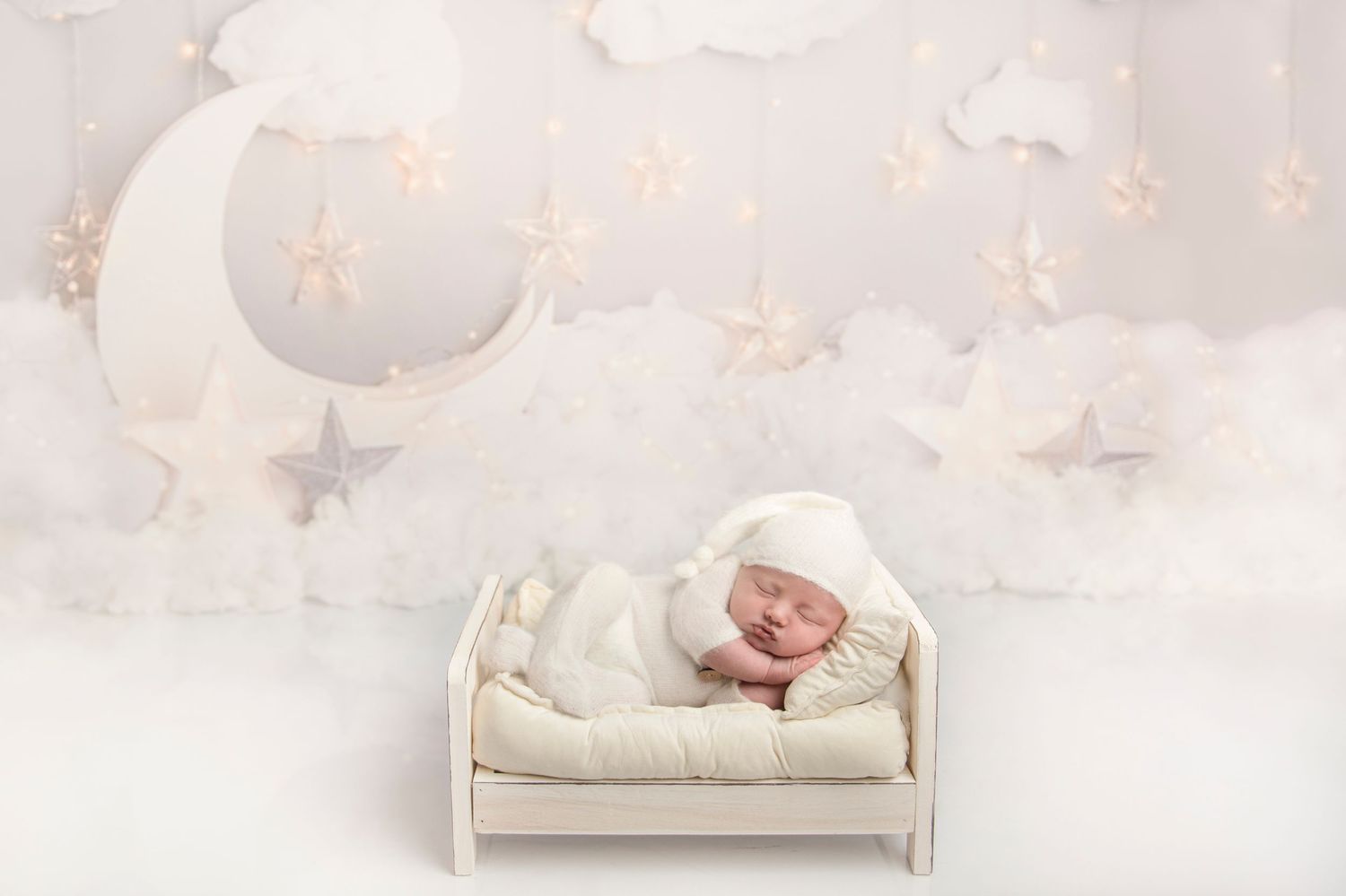 Ethereal newborn portrait with glowing fairy lights and white bedding.