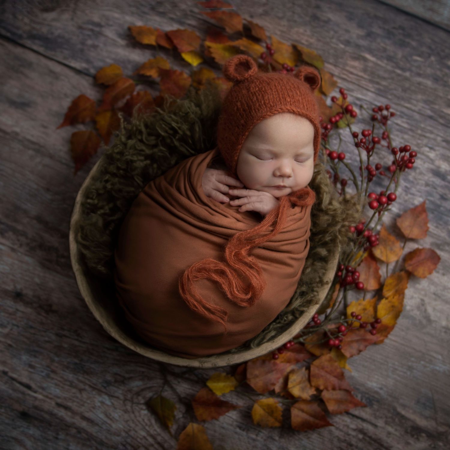 Autumn-themed newborn photography with rustic wood, fall leaves, and terracotta wrapping.