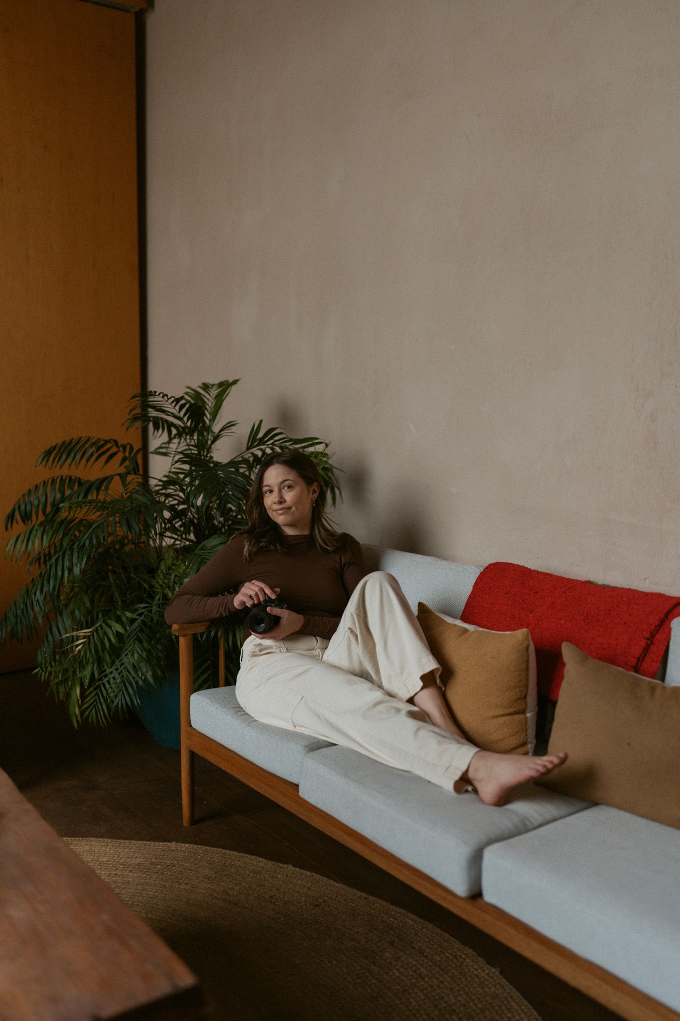 Woman relaxing on a modern sofa with colorful pillows beside an indoor plant.