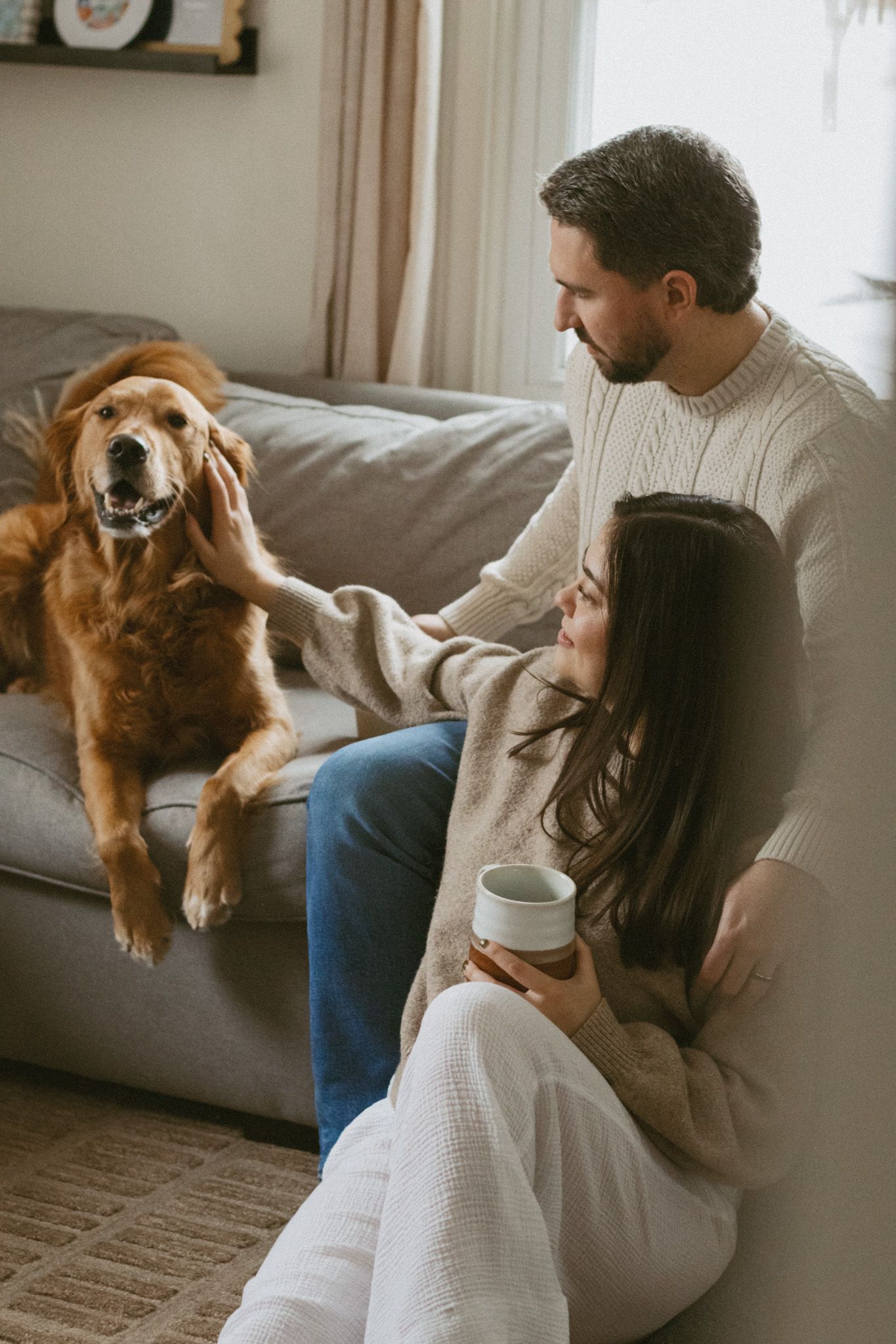 Couple relaxing on the floor with a golden retriever on a cozy couch in a warm living room.