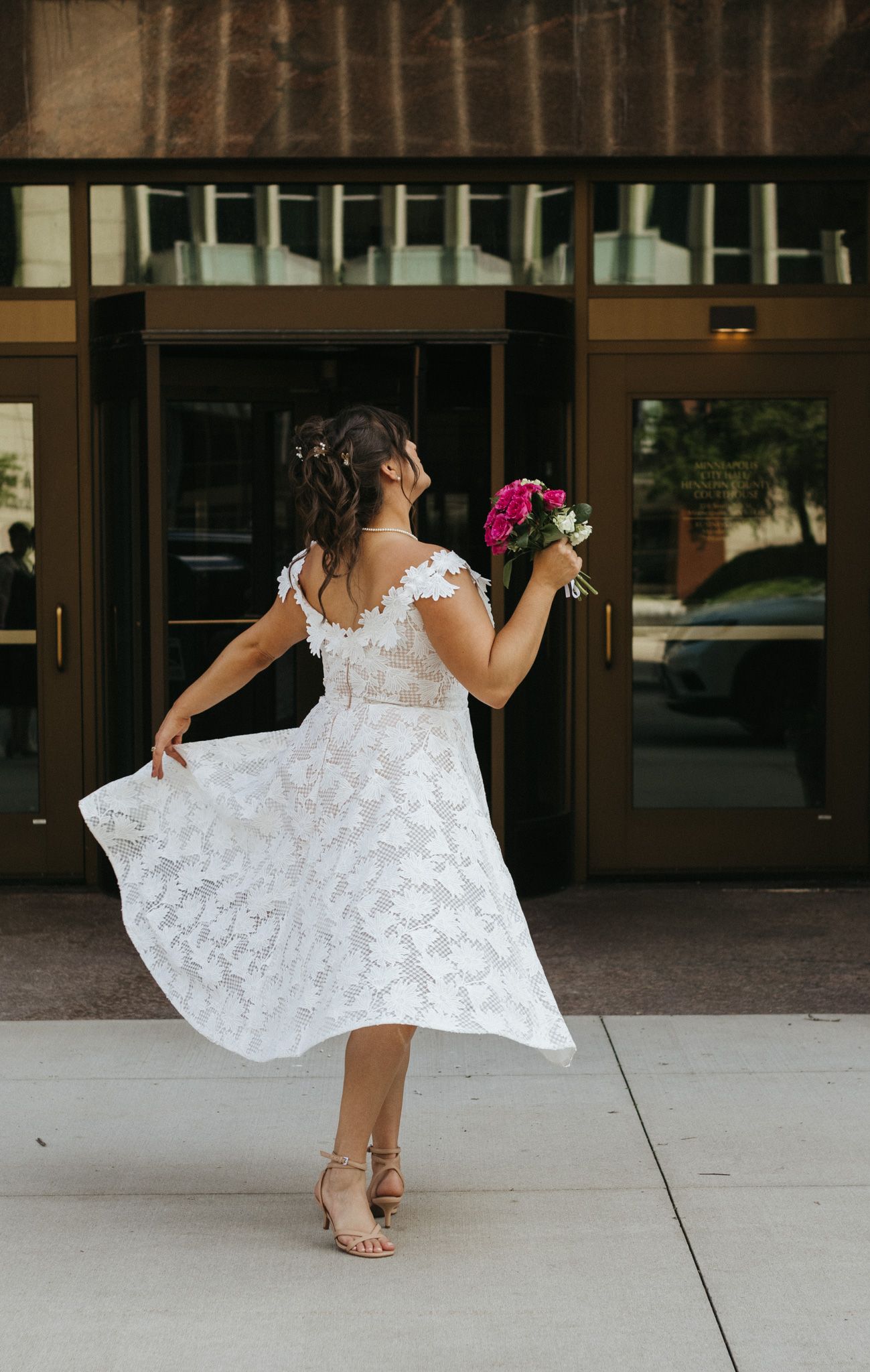 A bride twirls in a white lace dress and pink bouquet.