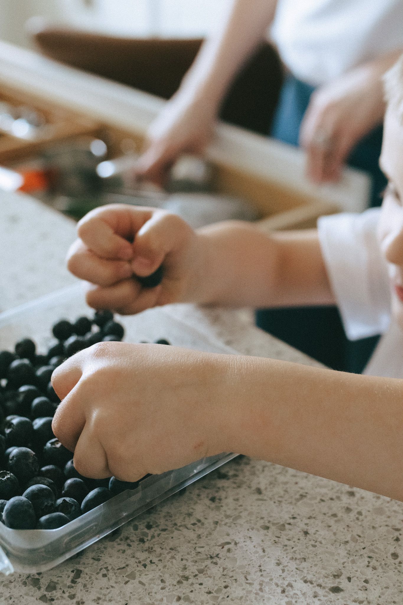 A child's hands reaching to steal blueberries.