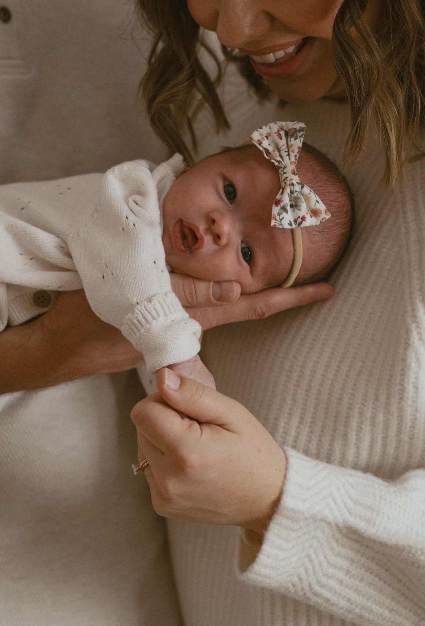 Close-up of a newborn baby girl in white outfit with floral bow headband.